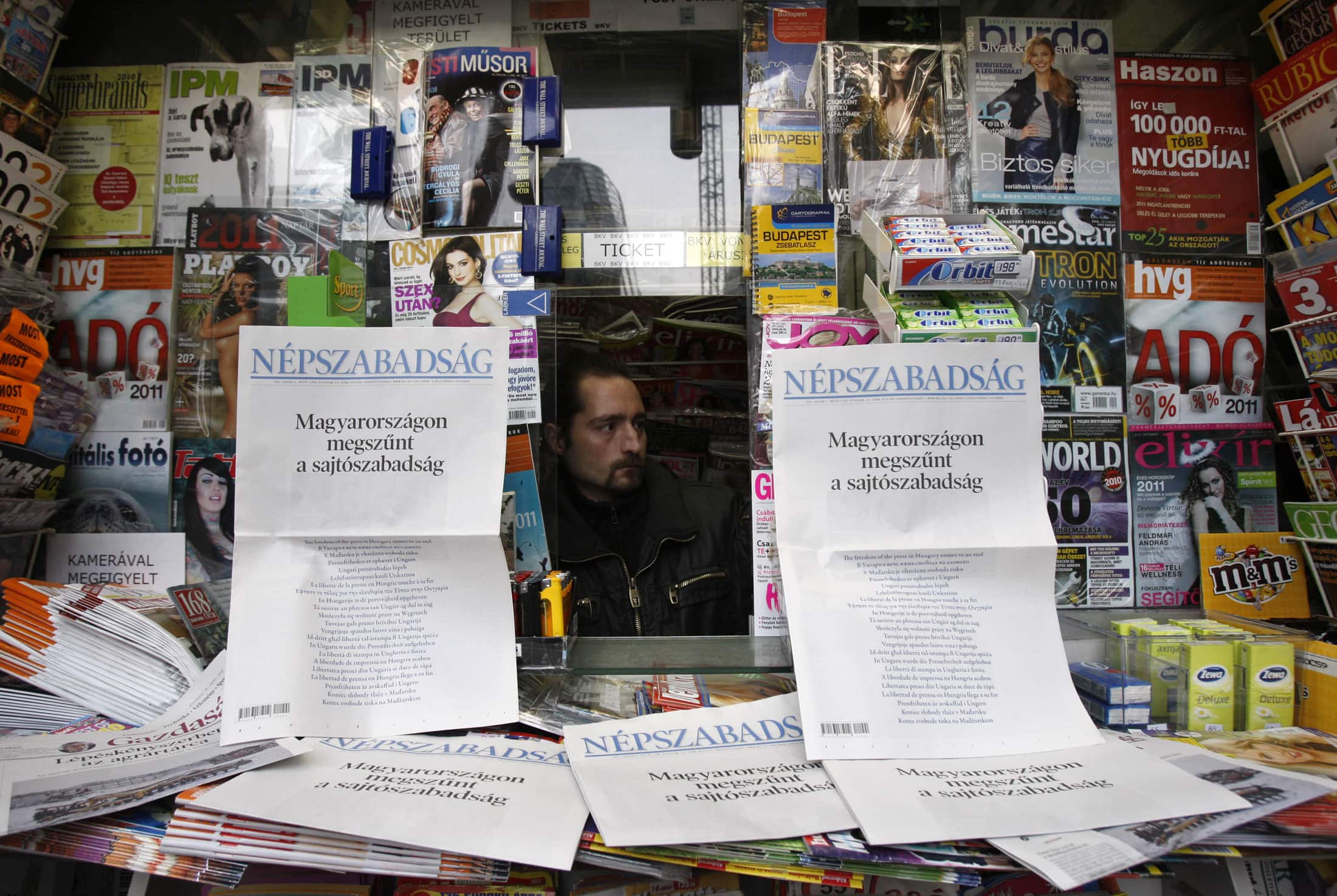 A news agent looks out from behind a spread of two Hungarian dailies which carried protests on their front pages against a new media law in Budapest, 3 January 2011, REUTERS/Bernadett Szabo