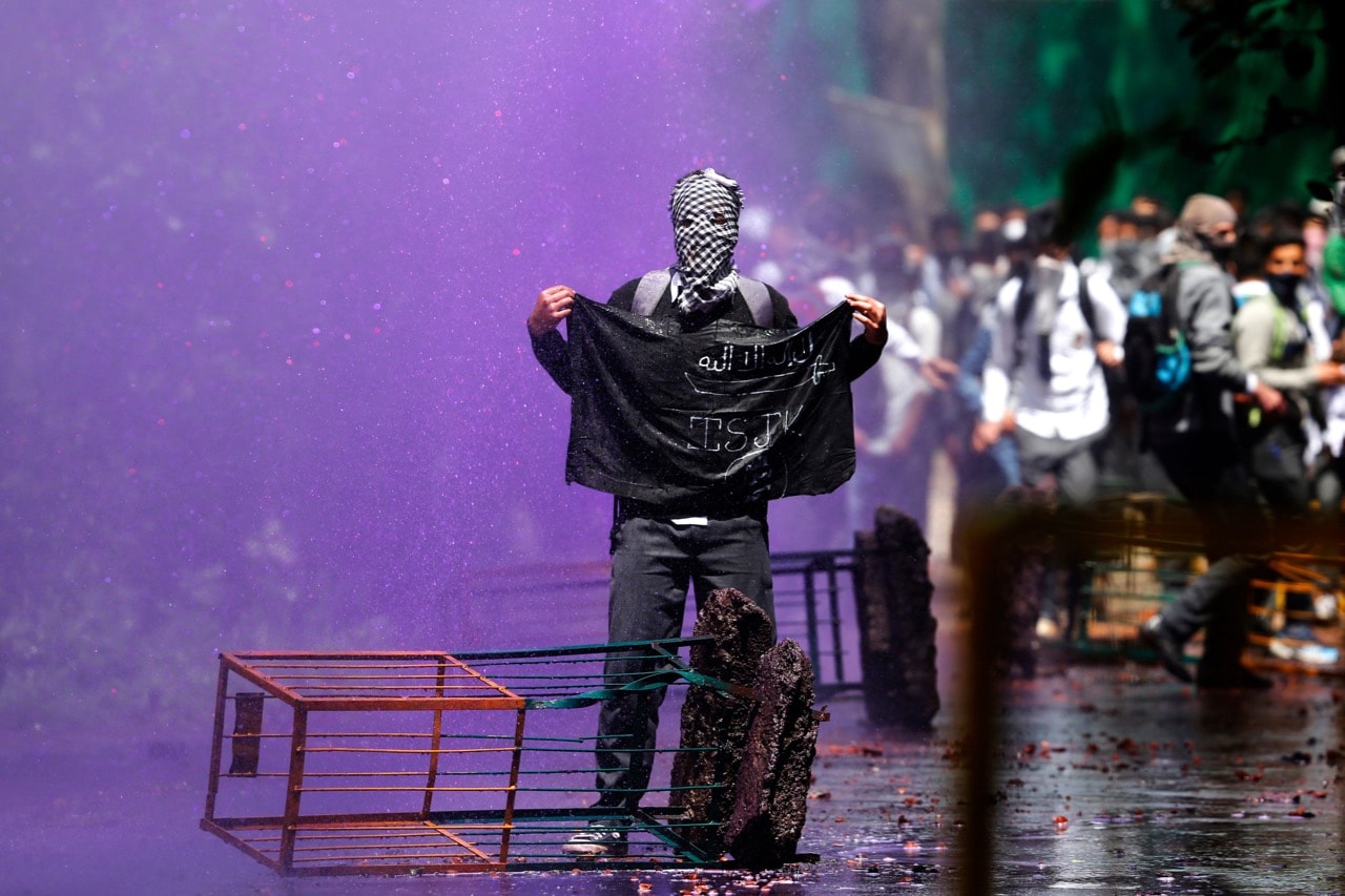 A Kashmiri student holds a black flag as Indian police use coloured water to disperse them in Srinagar, 24 April 2017, AP Photo/Mukhtar Khan