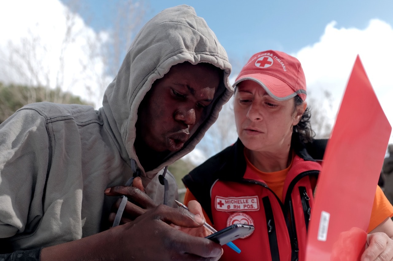 A migrant makes a call with the help of a member of the Italian Red Cross outside the 'Tracing Bus', a mobile office giving people the opportunity to re-establish a link with their families, in Rome, 6 March 2017, ALBERTO PIZZOLI/AFP/Getty Images