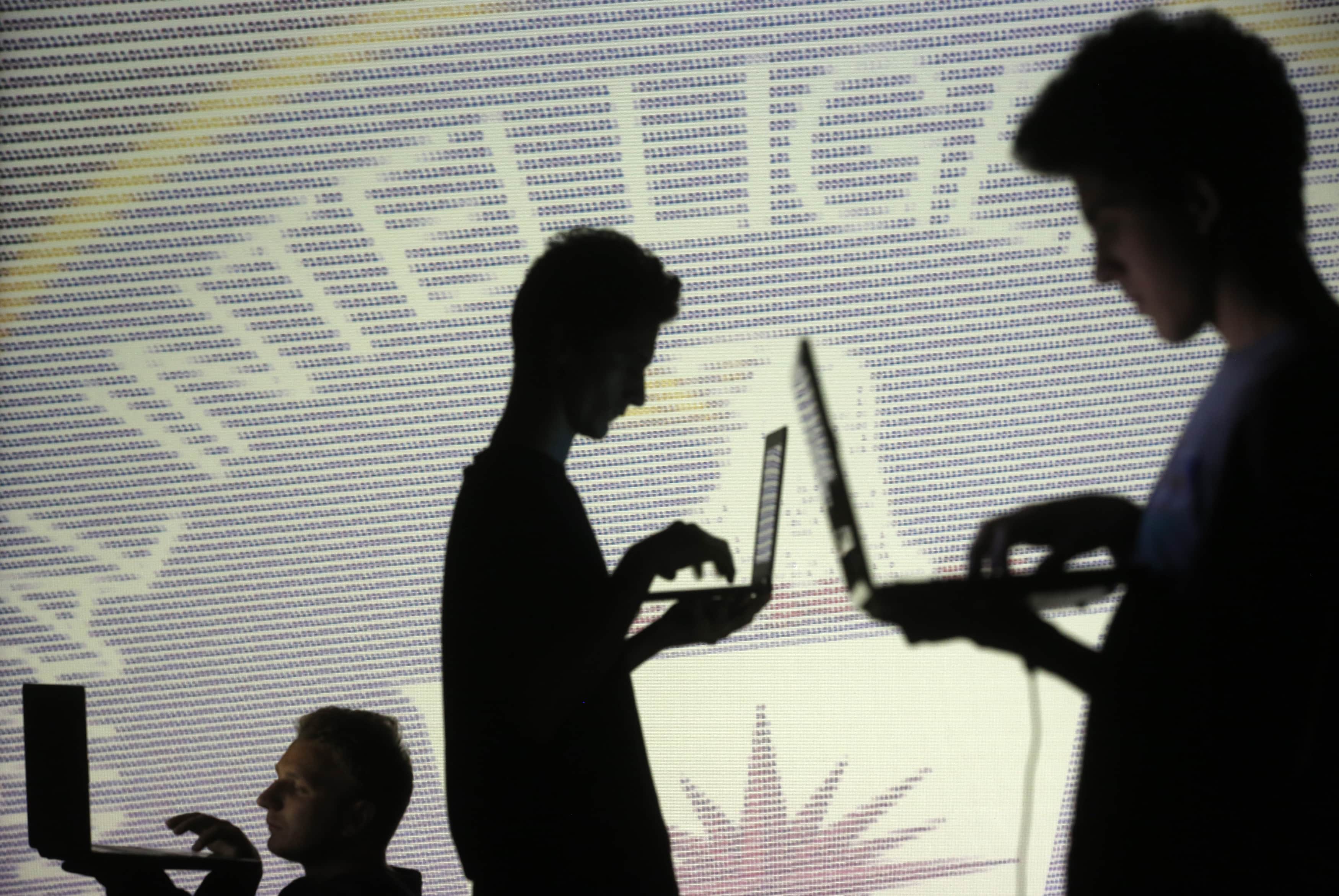 People are silhouetted as they pose with laptops in front of a screen projected with binary code and a CIA emblem, in Zenica, Bosnia, 29 October 2014, REUTERS/Dado Ruvic