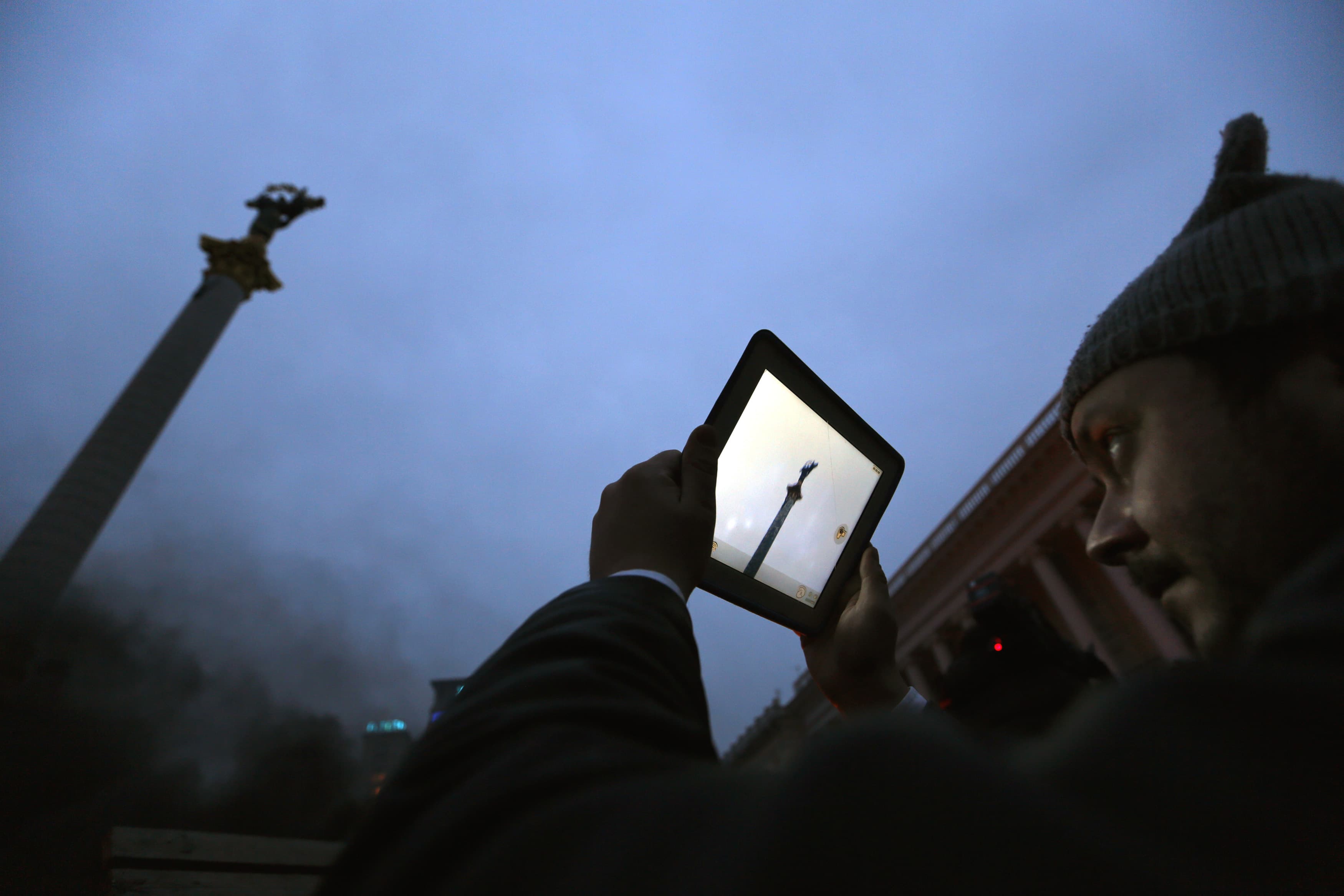 An anti-government protester takes pictures as he stands behind burning barricades in Kiev's Independence Square, 19 February 2014, REUTERS/Yannis Behrakis