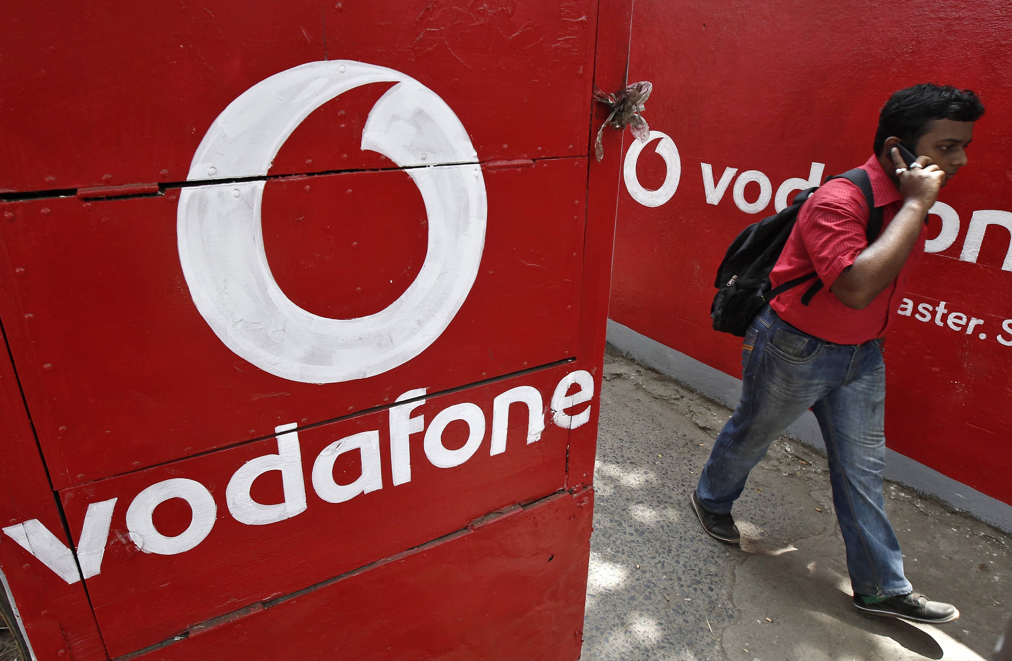 A man speaks on his mobile phone as he walks past logos of Vodafone painted on a roadside wall in Kolkata, India, 20 May 2014, REUTERS/Rupak De Chowdhuri