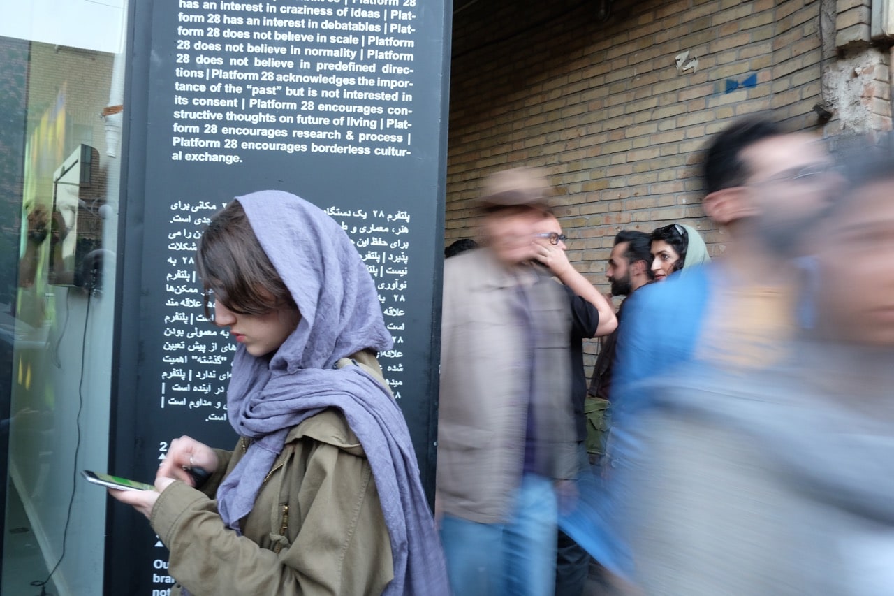 A young woman checks her smartphone as people pass by on a busy street in the old part of the city of Tehran, Iran, 21 April 2017, Kaveh Kazemi/Getty Images