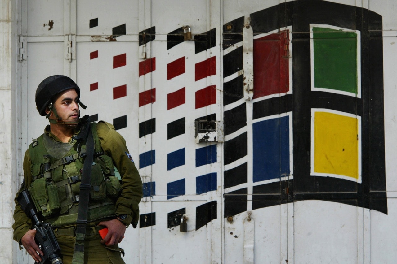 In this 7 February 2003 file photo, an Israeli soldier stands in front of a closed computer store as he conducts document checks of Palestinians in the southern West Bank town of Hebron, AP Photo/Lefteris Pitarakis, File