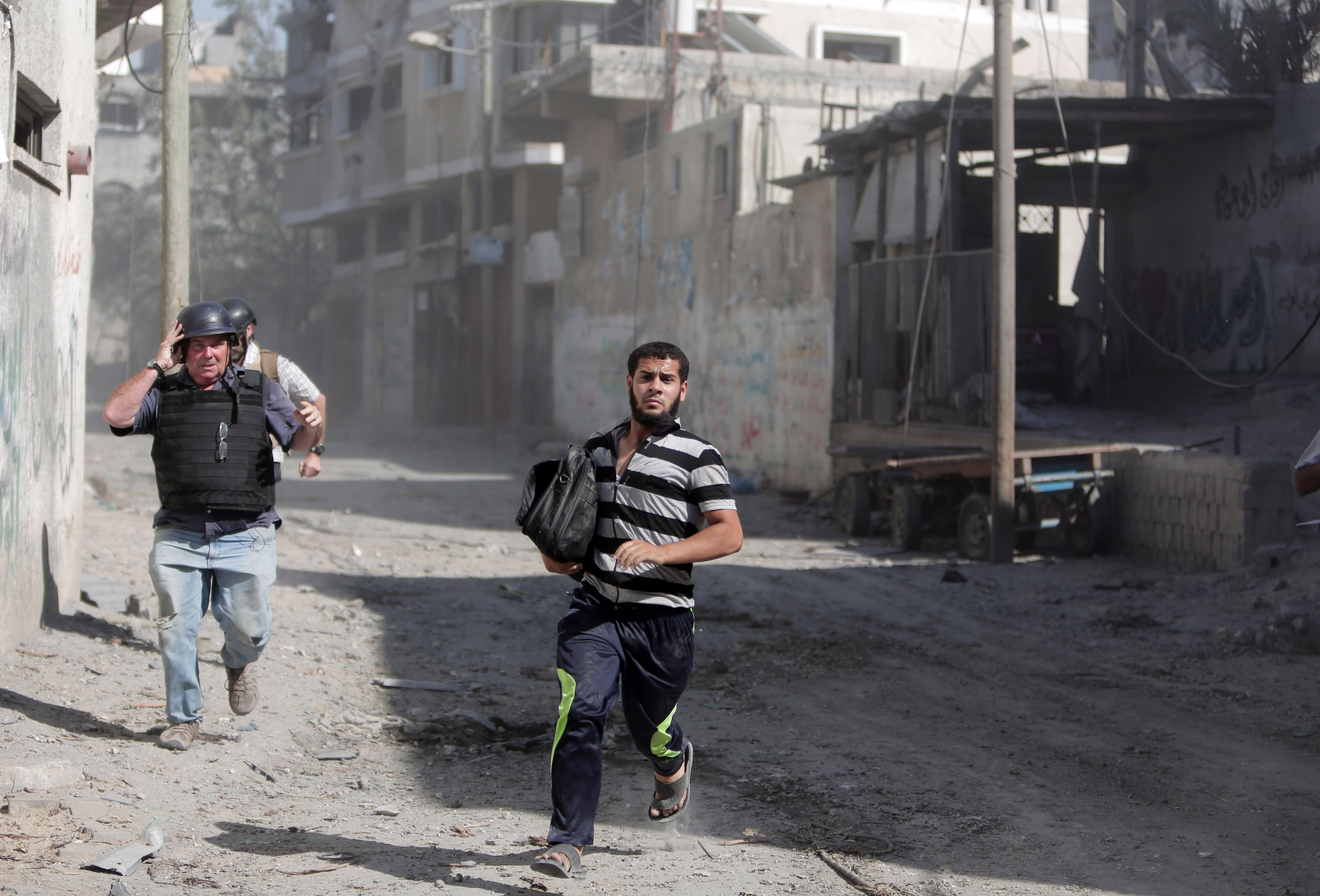 Palestinian residents and journalists run for cover from gunfire during a two hour temporary ceasefire in Gaza City's Shijaiyah neighborhood on 23 July 2014, AP Photo/Khalil Hamra