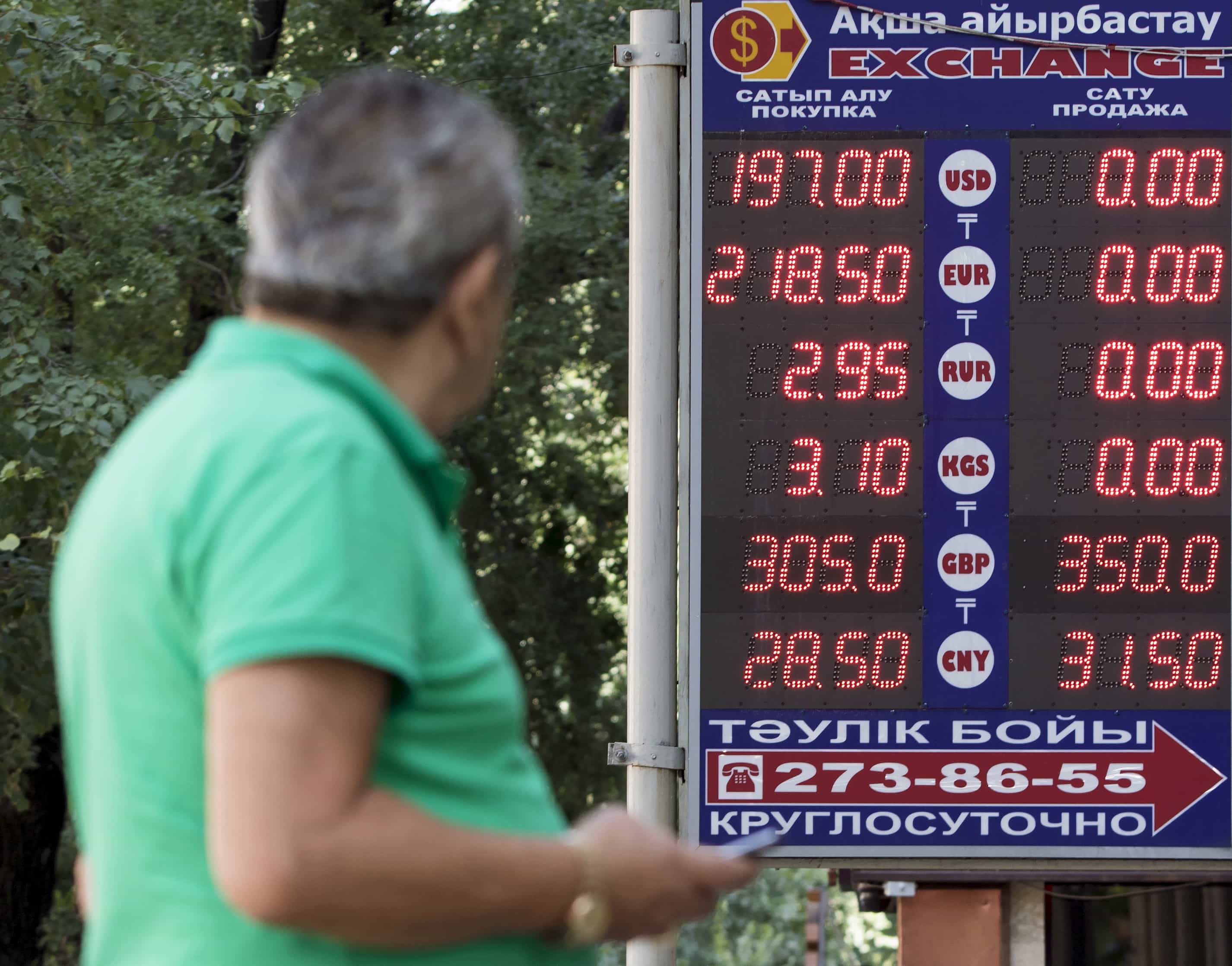 A man uses his mobile phone as he walks past a board showing currency exchange rates in Almaty, 20 August 2015, REUTERS/Pavel Mikheyev