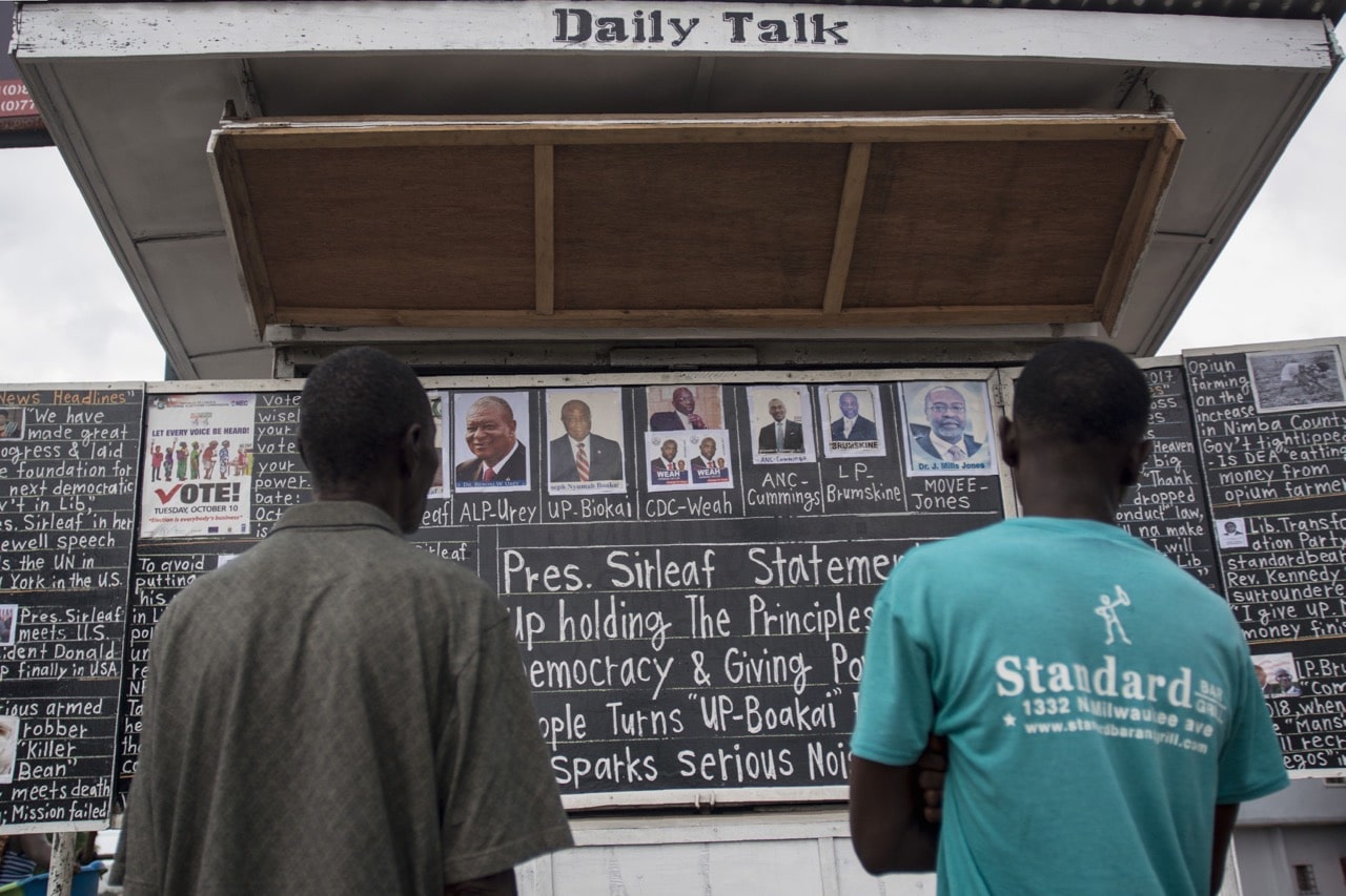 People stand in front of the "Daily Talk" chalkboard on Tubman Boulevard, in Monrovia, Liberia, 27 September 2017, CRISTINA ALDEHUELA/AFP/Getty Images