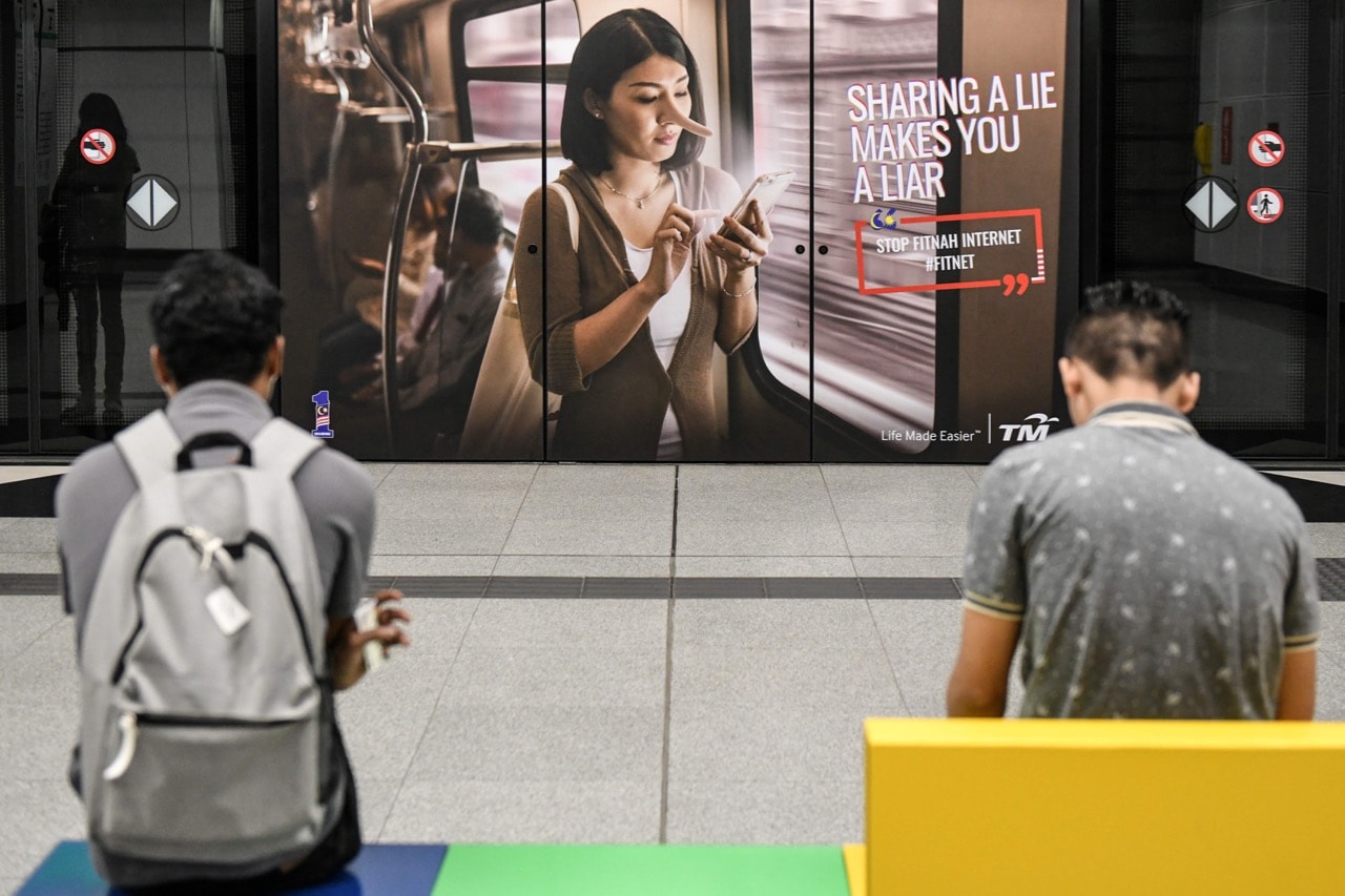 Commuters wait for the train in front of a government advertisement about 'fake news', at a station in Kuala Lumpur, Malaysia, 26 March 2018, MOHD RASFAN/AFP/Getty Images