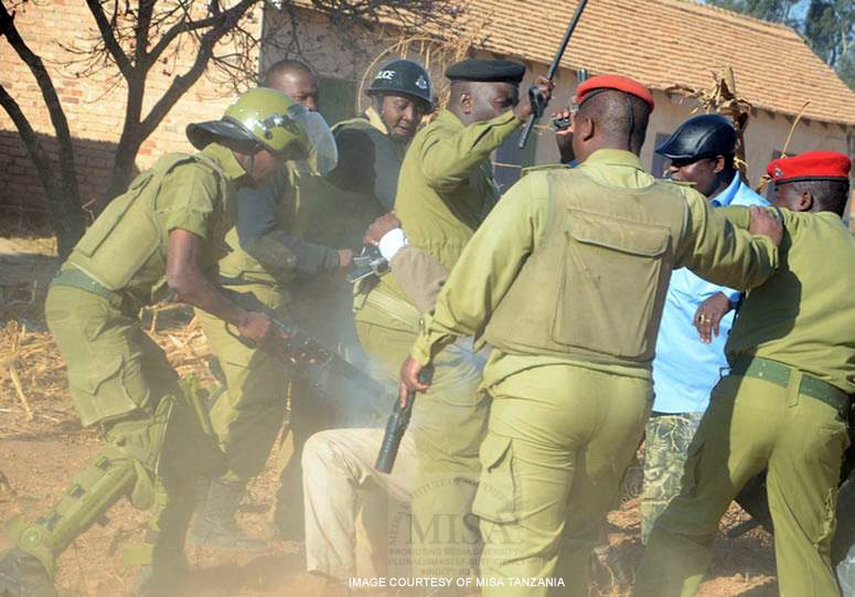 A police officer points a rifle at a person being held down by other officers, MISA Tanzania