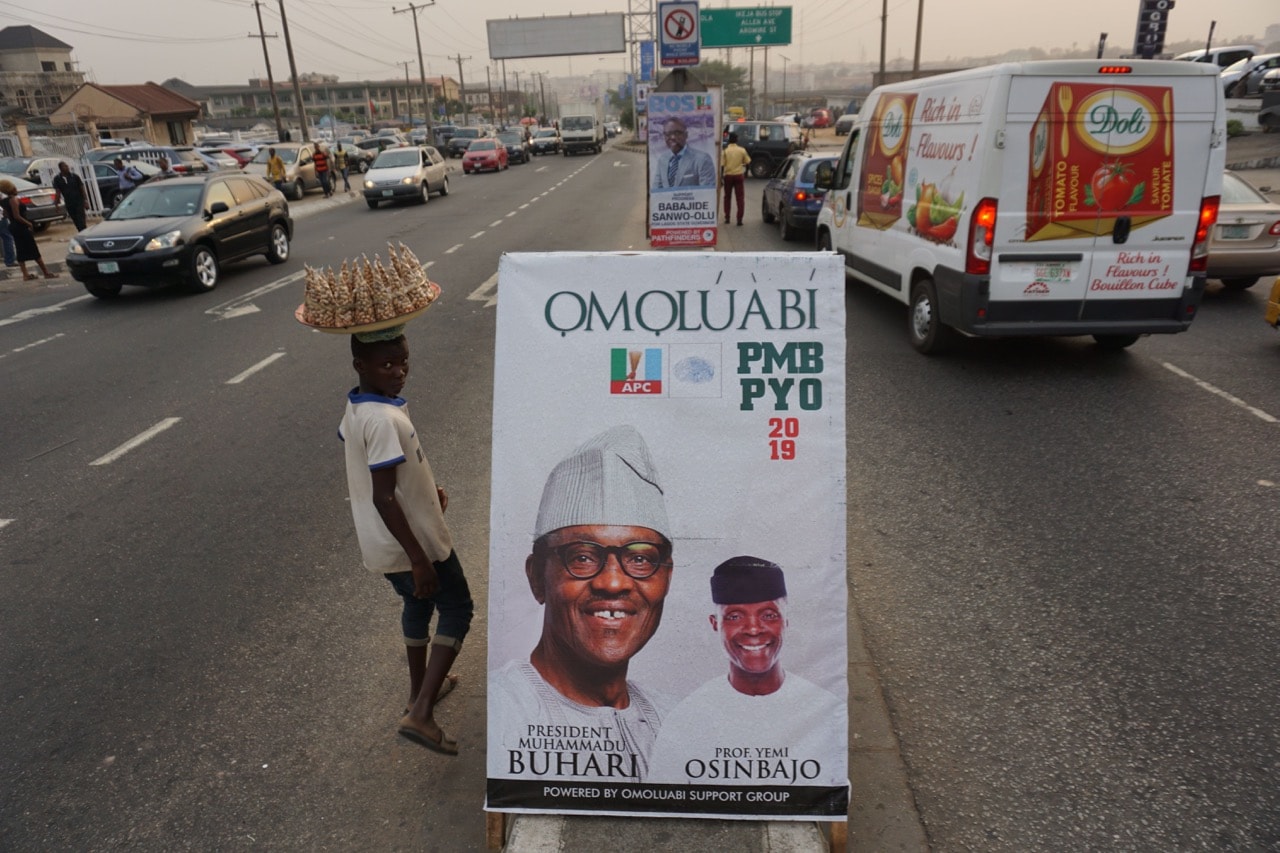 A young vendor walks past a campaign poster of the candidates for the ruling APC party, on a road at Ikeja in Lagos, Nigeria, 10 December 2018, PIUS UTOMI EKPEI/AFP/Getty Images