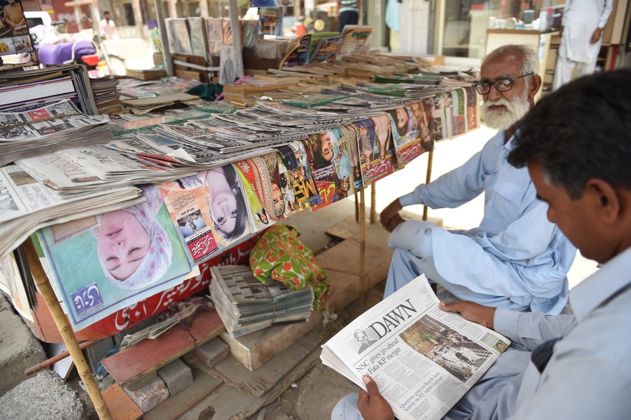 A man reads a copy of the "Dawn" English-language newspaper at a newspaper stall in Karachi, Pakistan, 20 May 2018, RIZWAN TABASSUM/AFP/Getty Images