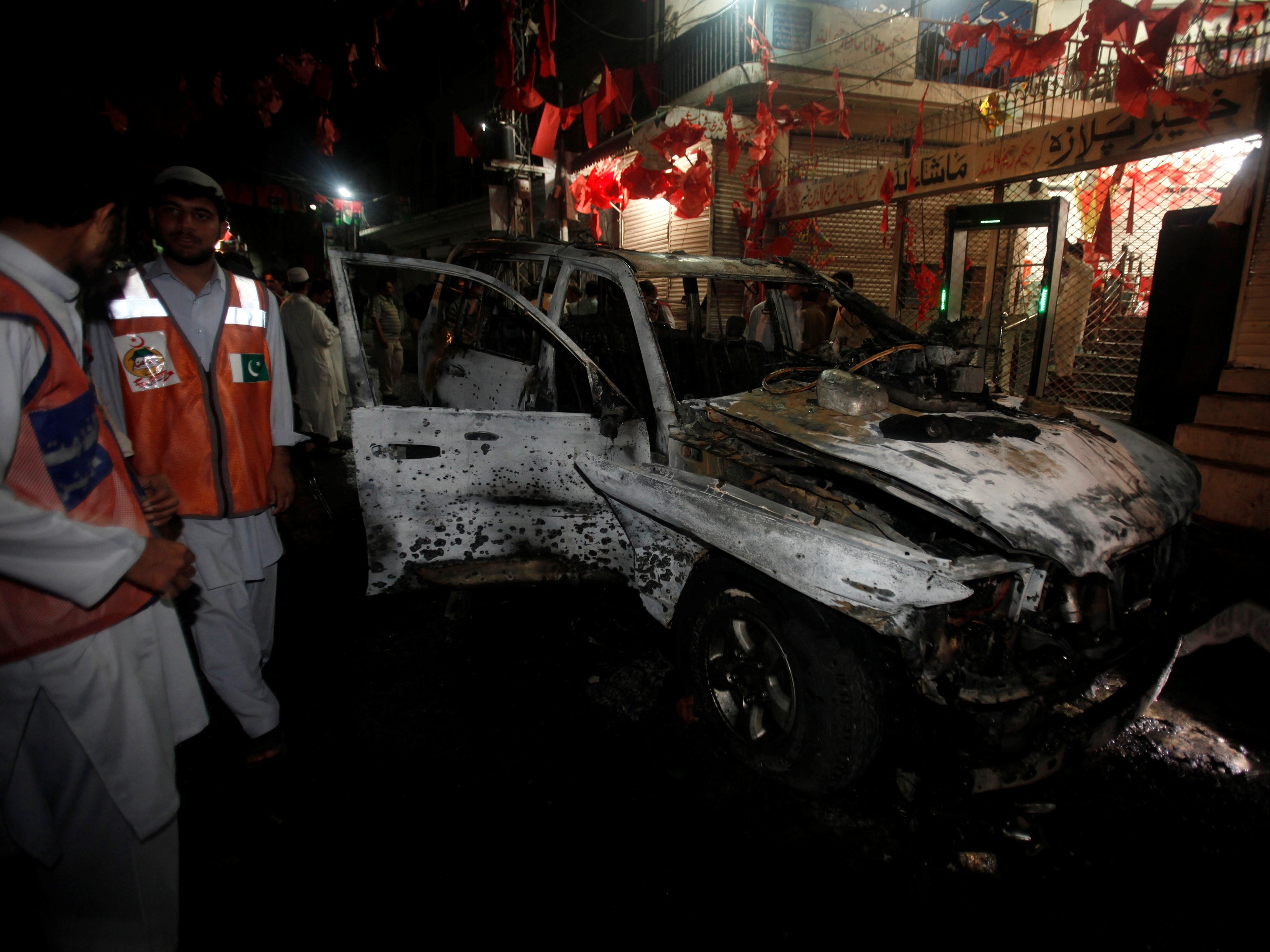 Rescue workers stand near a damaged vehicle at the site of the suicide bomb attack in Peshawar, 16 April 2013, REUTERS/Fayaz Aziz