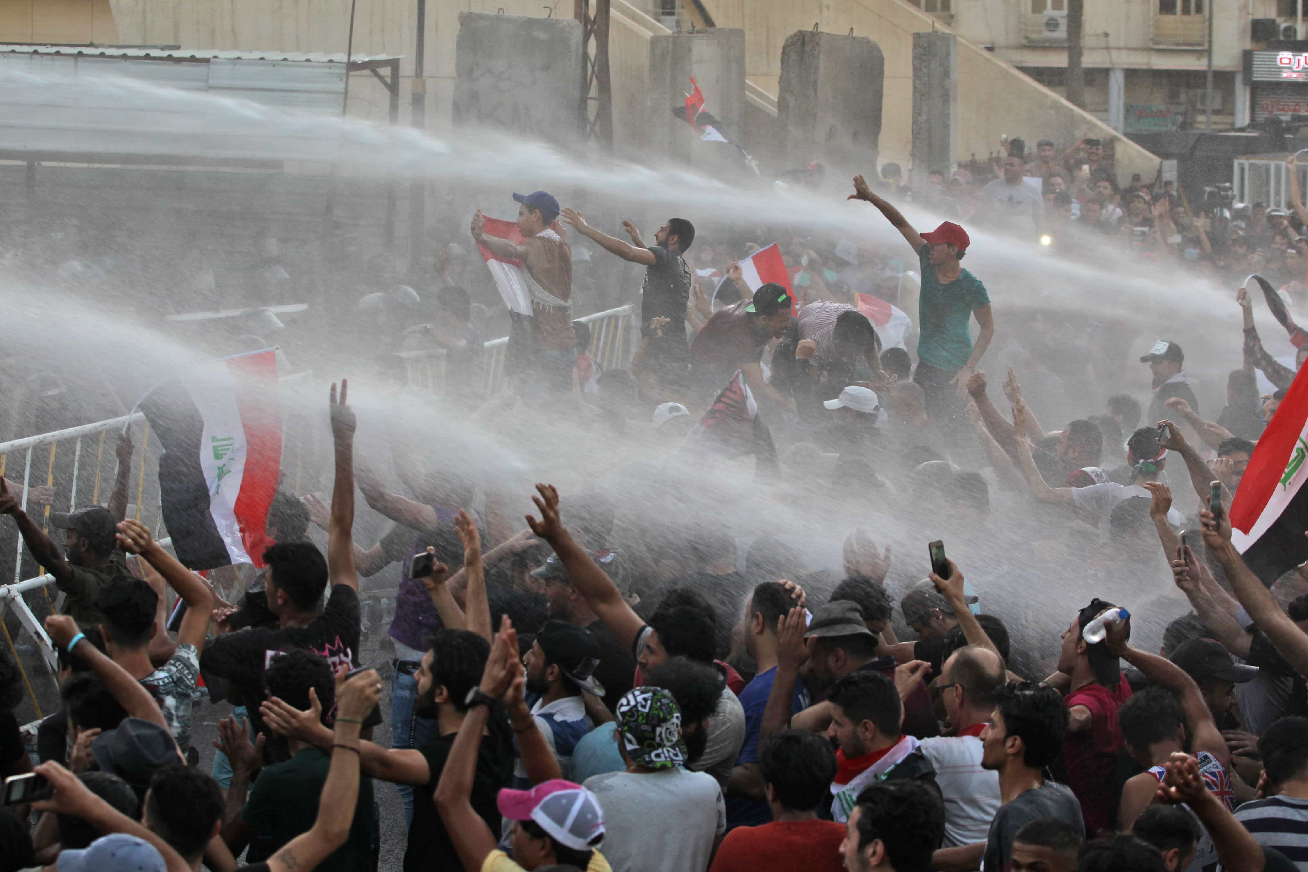 Protesters waving national flags are sprayed with water cannon by security forces, Baghdad, Iraq, 20 July 2018, AHMAD AL-RUBAYE/AFP/Getty Images