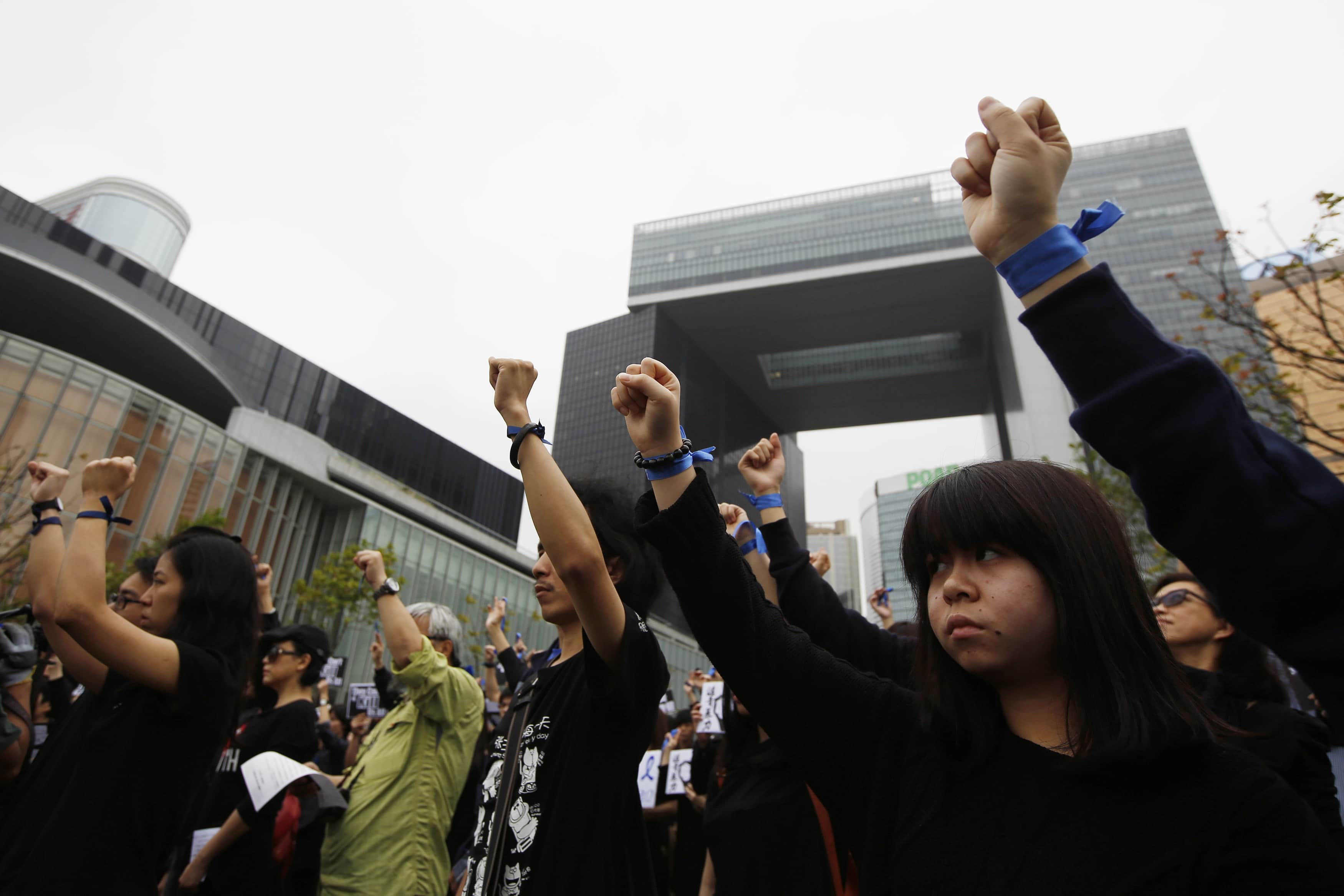 Protesters raise their fists with a blue ribbon during the "Standing in Silent Action" event in support of the Hong Kong Journalist Association (HKJA) at Tamar Park in Hong Kong, 2 March 2014, REUTERS/Tyrone Siu