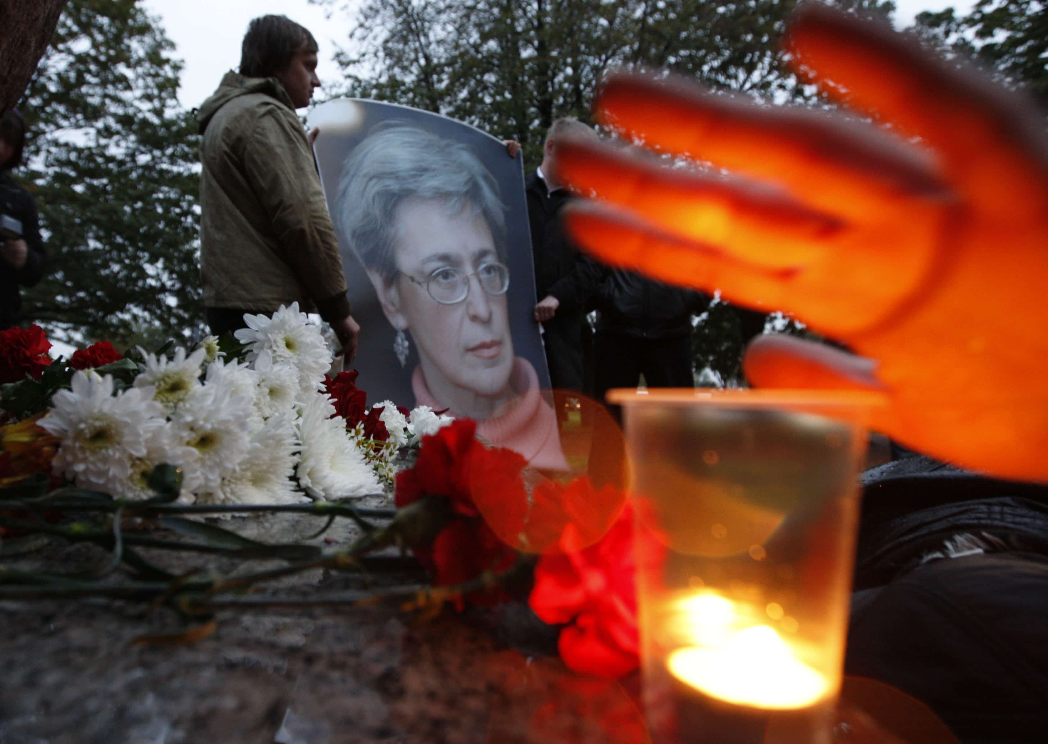 A man holds a portrait of the killed journalist Anna Politkovskaya as a woman lights up a candle during a commemorative rally in St.Petersburg, October 7, 2009., REUTERS/Alexander Demianchuk