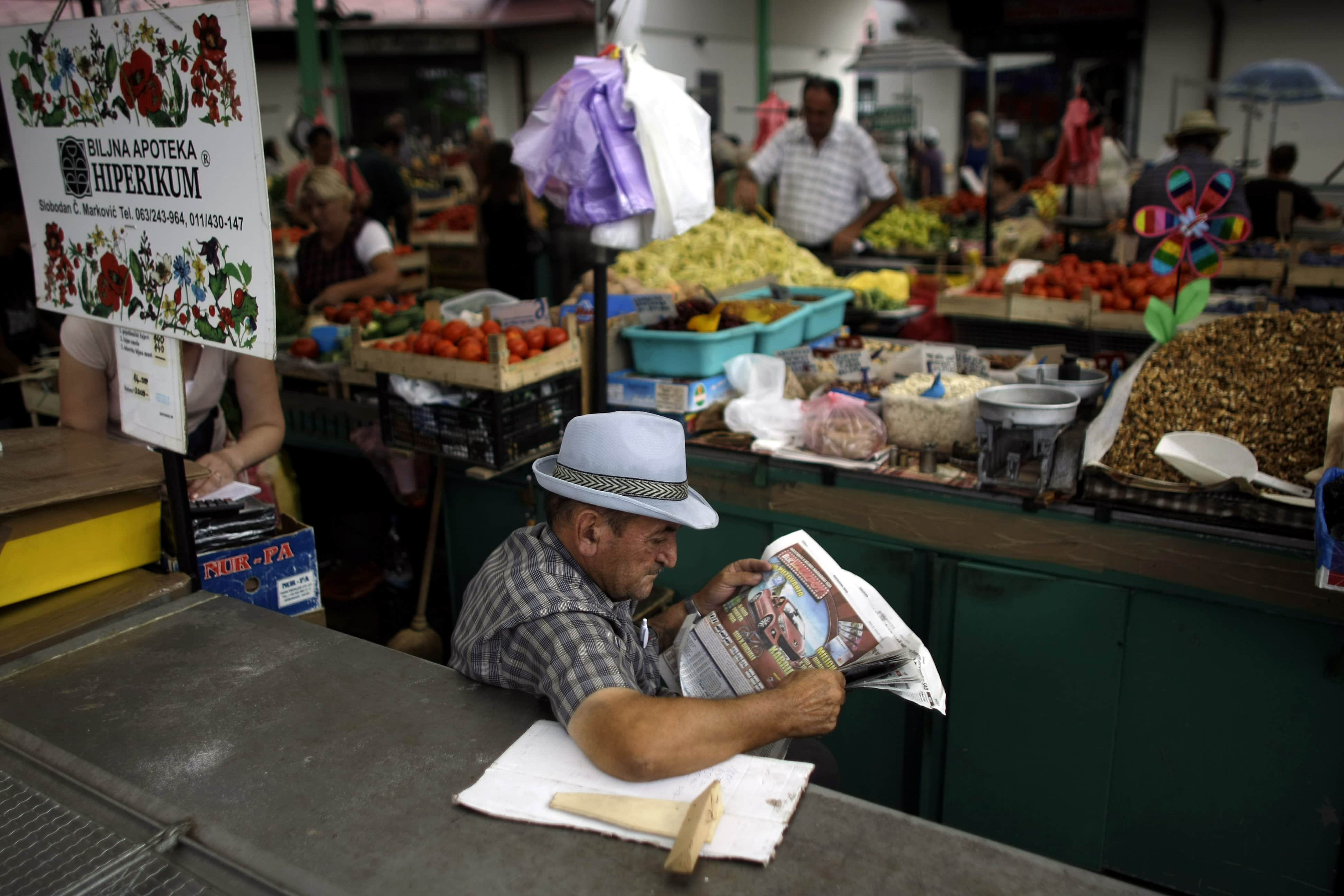 A vendor reads a newspaper while waiting for customers at an open air market in Belgrade, Serbia, 10 August 2010, AP Photo/Marko Drobnjakovic