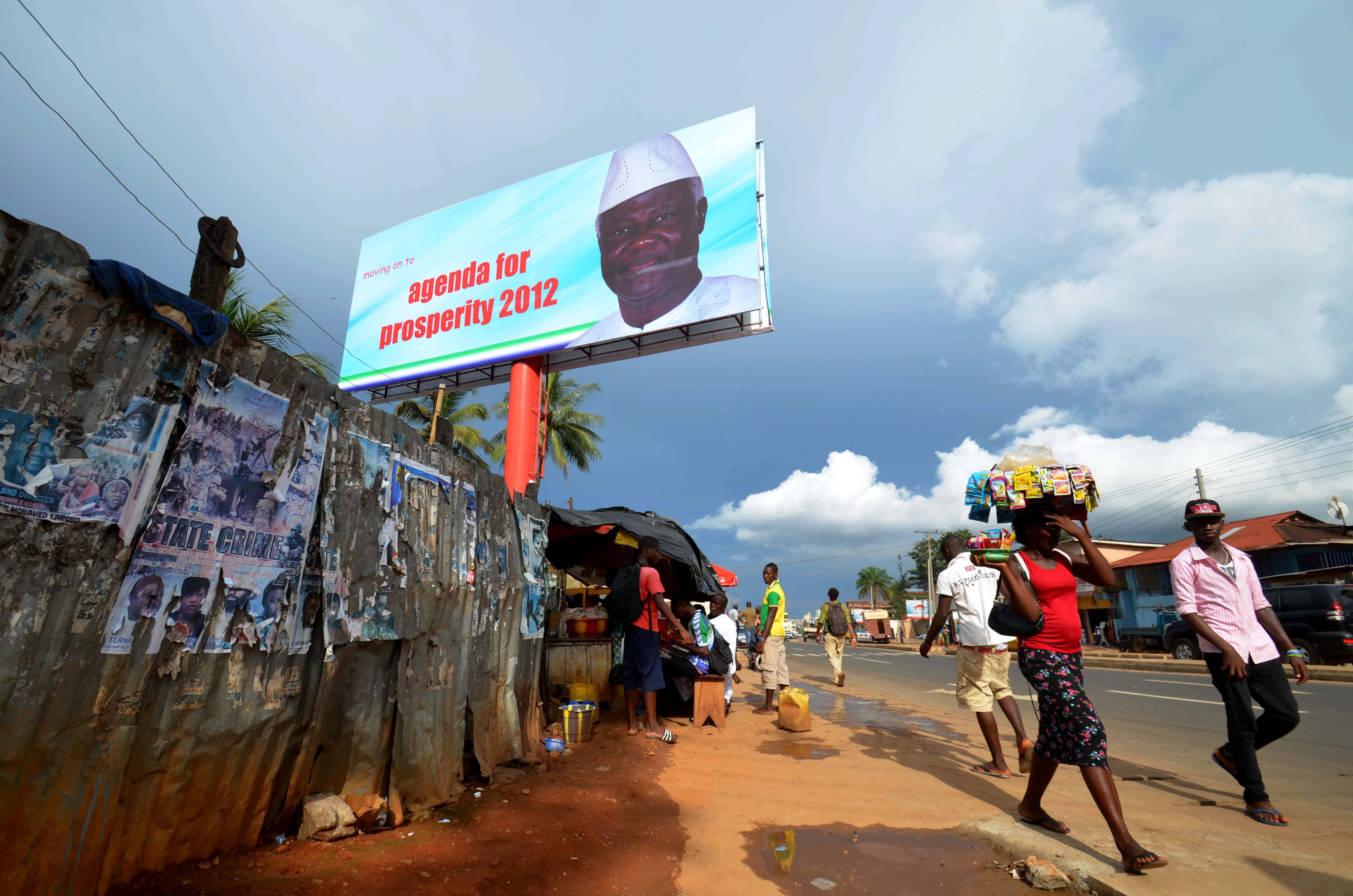 People walk past a campaign poster for President Ernest Bai Koroma. Two Sierra Leonean editors are currently facing charges for "defaming" the president in a recent news article., AP Photo/Tommy Trenchard