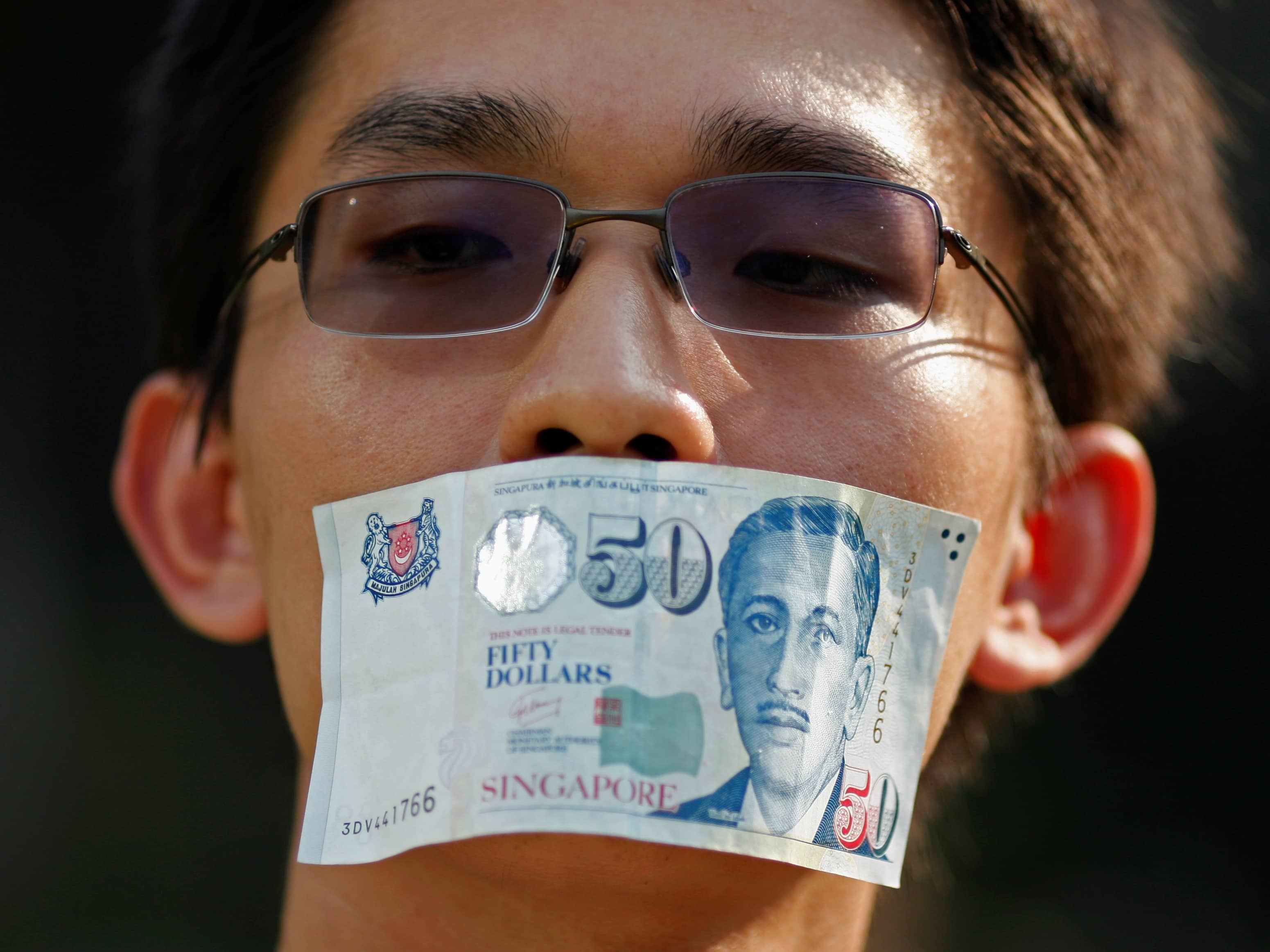 A man covers his mouth with a Singaporean 50 dollar note (US$40) during a protest in Singapore against new licensing regulations imposed by the government for online news sites, 8 June 2013, REUTERS/Edgar Su