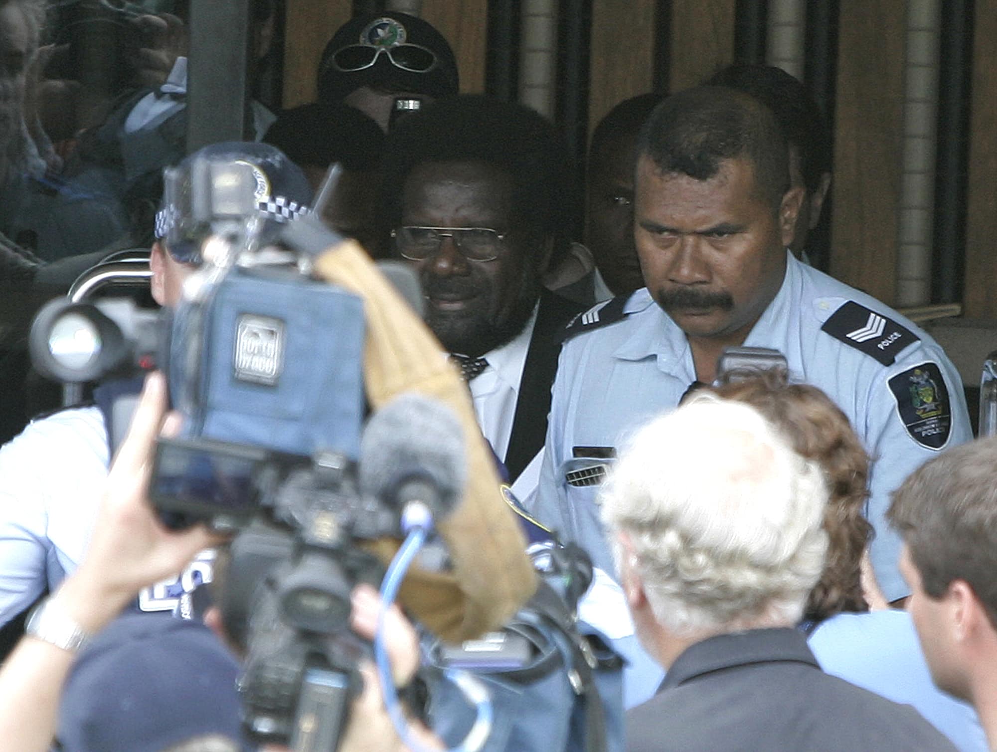 In this 26 April 2006 file photo, caretaker prime minister Snyder Rini, center, at parliament house in Honiara in the Solomon Islands, is escorted through a media pack by armed police, AP Photo/Rob Griffith