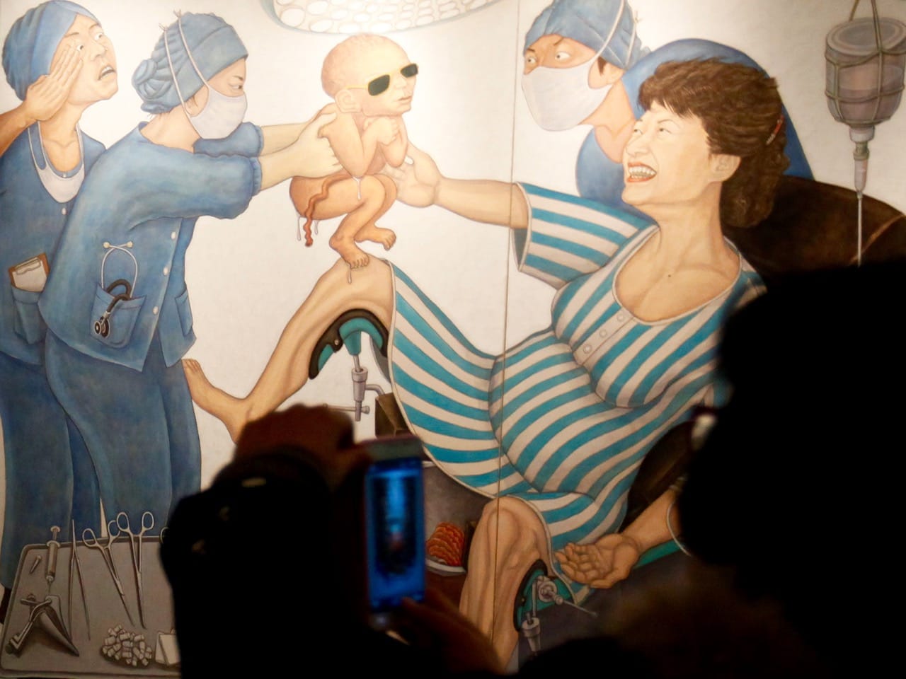 A visitor takes pictures of a painting by artist Hong Song-dam at the Space99 Gallery in Seoul, 20 November 2012. The painting depicts Park Geun-hye as a mother giving birth to a baby Park Chung Hee, her father, REUTERS/Kim Hong-ji