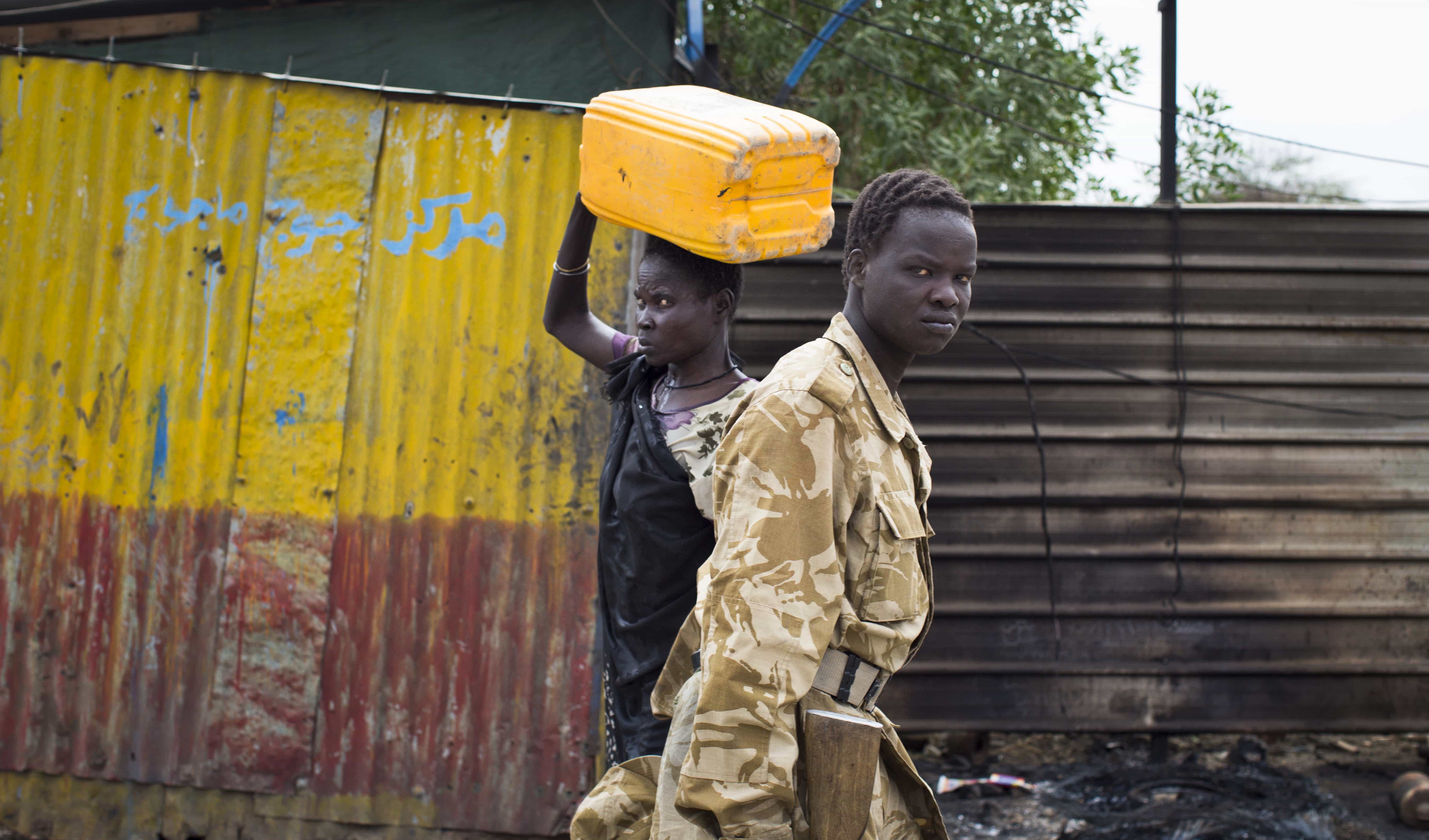 A South Sudanese government soldier and a woman carrying a container pass each other in the street in Malakal, Upper Nile State, in South Sudan, 21 January 2014., AP Photo/Mackenzie Knowles-Coursin