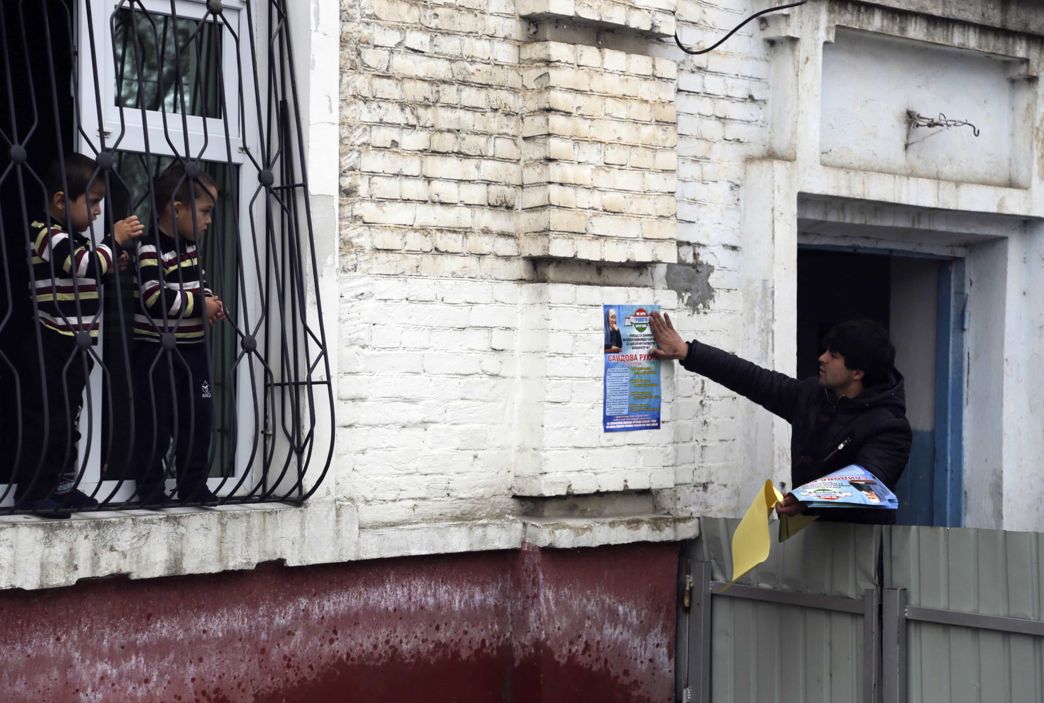 Children watch a supporter of the Islamic Renaissance Party of Tajikistan (IRPT) pasting a campaign poster on a wall in the Tajik capital, Dushanbe, 26 February 2015, REUTERS/Nozim Kalandarov