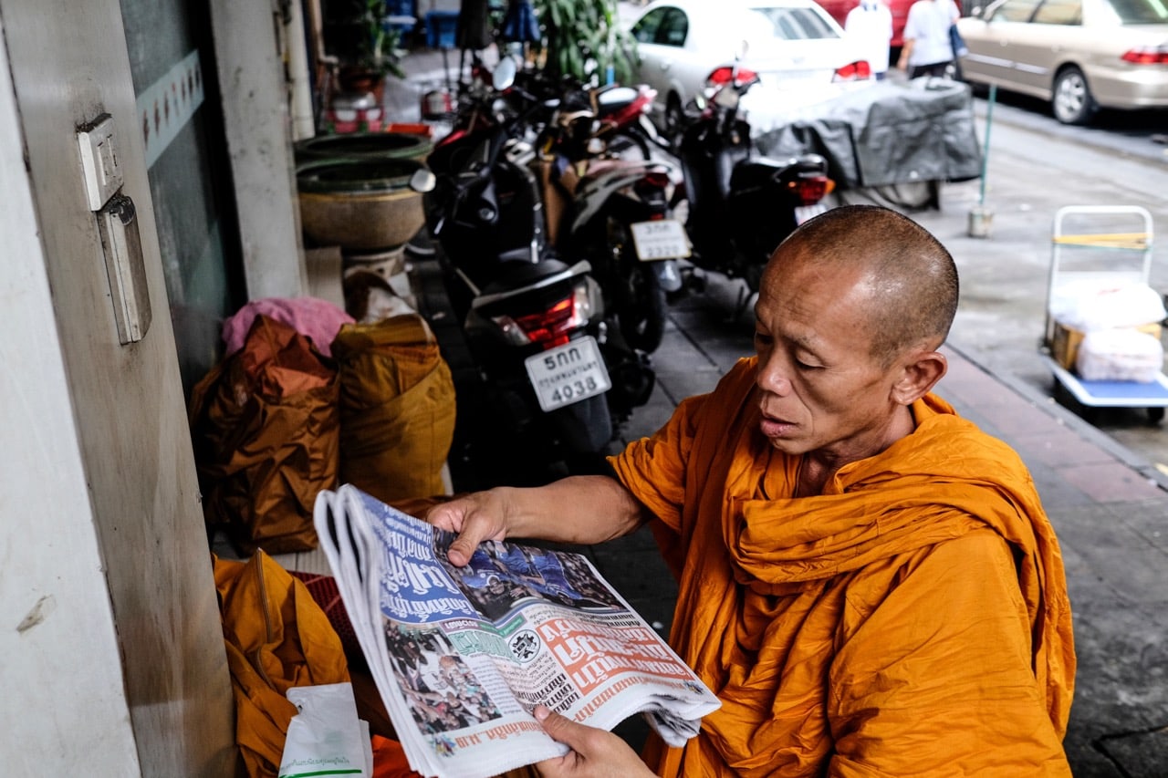 A Thai Buddhist monk reads a newspaper as he waits for others to join him during his morning walk, Bangkok, 17 May 2017, David Longstreath/LightRocket via Getty Images