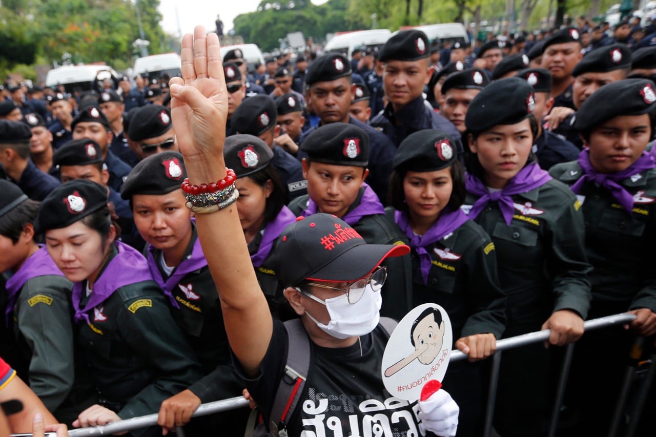 A Thai pro-democracy activist holds a fan with a caricature of Prime Minister Prayut Chan-o-cha with a Pinocchio nose and flashes the three-finger salute inspired by the movie "The Hunger Games" during a raly in Bangkok, 22 May 2018, Chaiwat Subprasom/NurPhoto via Getty Images