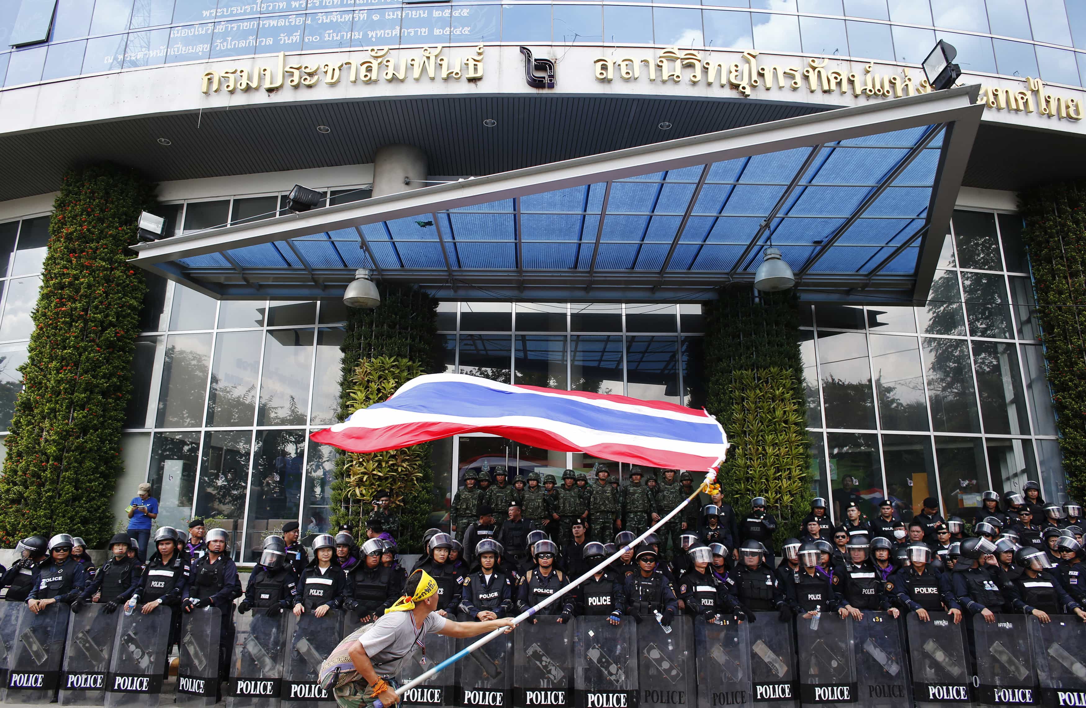 An anti-government protestor waves a national flag in front of riot police and soldiers guarding the National Broadcast Services of Thailand television station in Bangkok, 9 May 2014, REUTERS/Athit Perawongmetha