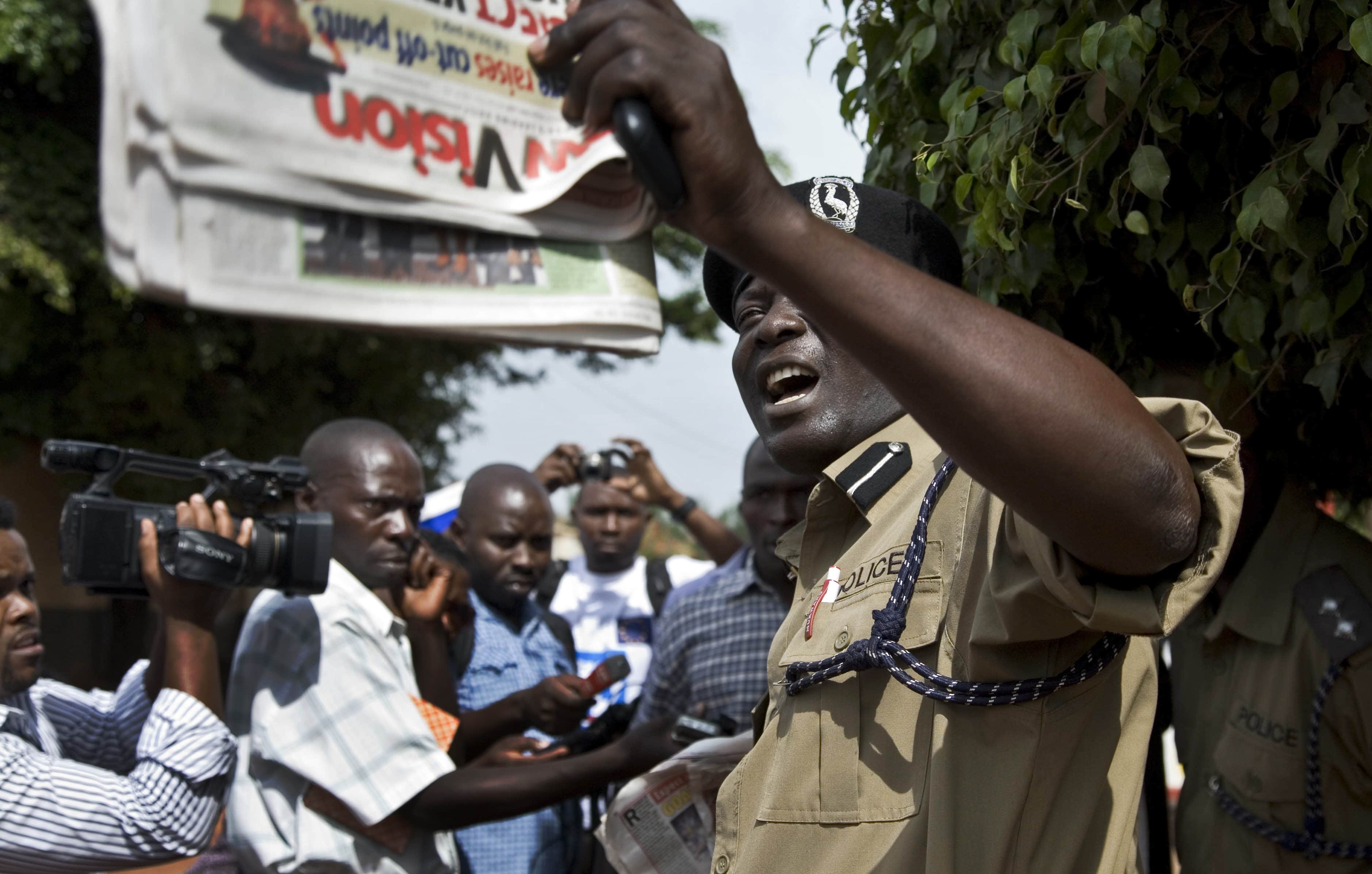 A Ugandan police officer holds up a newspaper as media protest outside the Daily Monitor newspaper head office, just before police fired tear gas to disperse the demonstration, in Kampala, Uganda, 28 May 2013, AP Photo/Rebecca Vassie, File