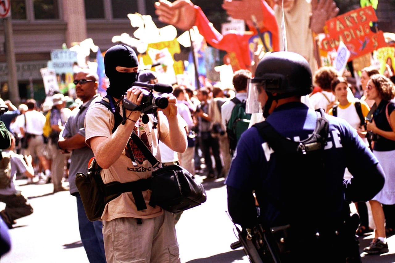 A disguised protestor videos an LAPD officer during the Democratic National Convention in Los Angeles, CA, 14 August 2000; as EFF notes, some regulations on violent content have disappeared documentation of police brutality, Dan Callister/Newsmakers