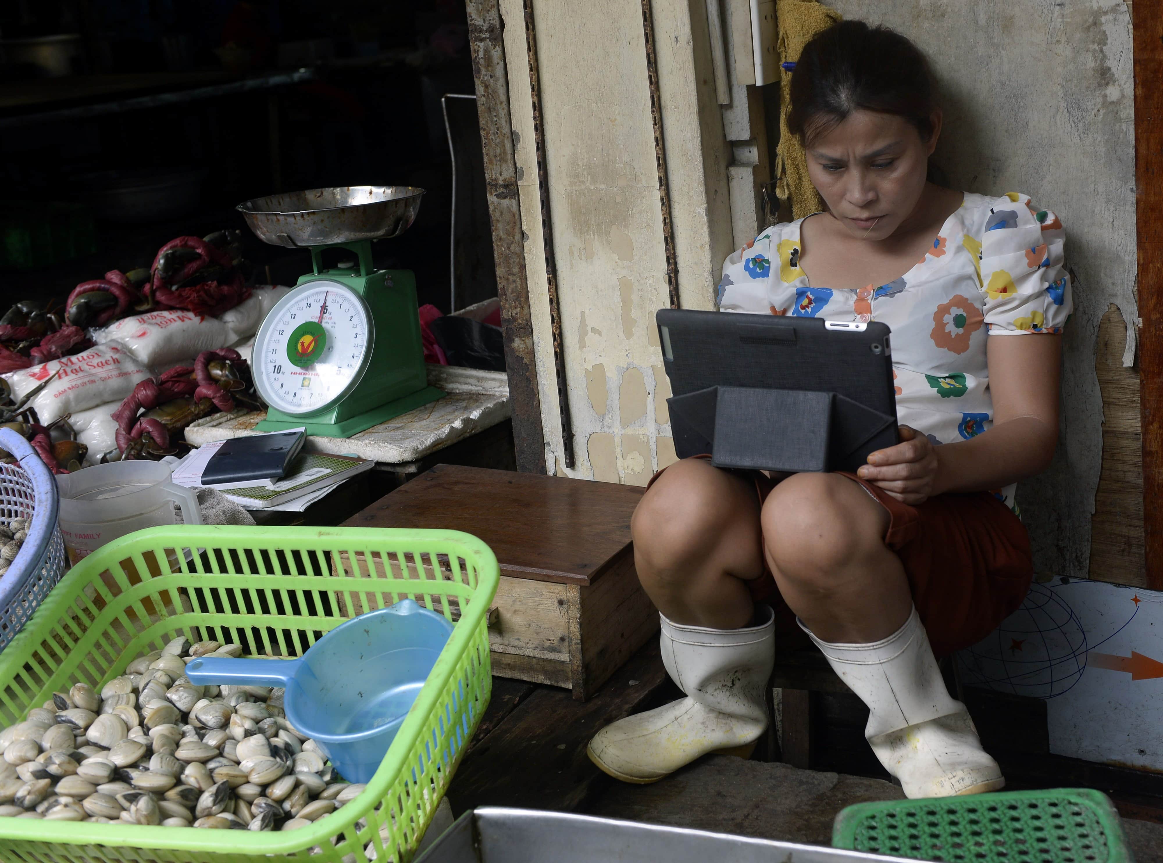 A seafood vendor using an iPad at her stand in a market, Hanoi, Vietnam, 2013, HOANG DINH NAM/AFP/Getty Images