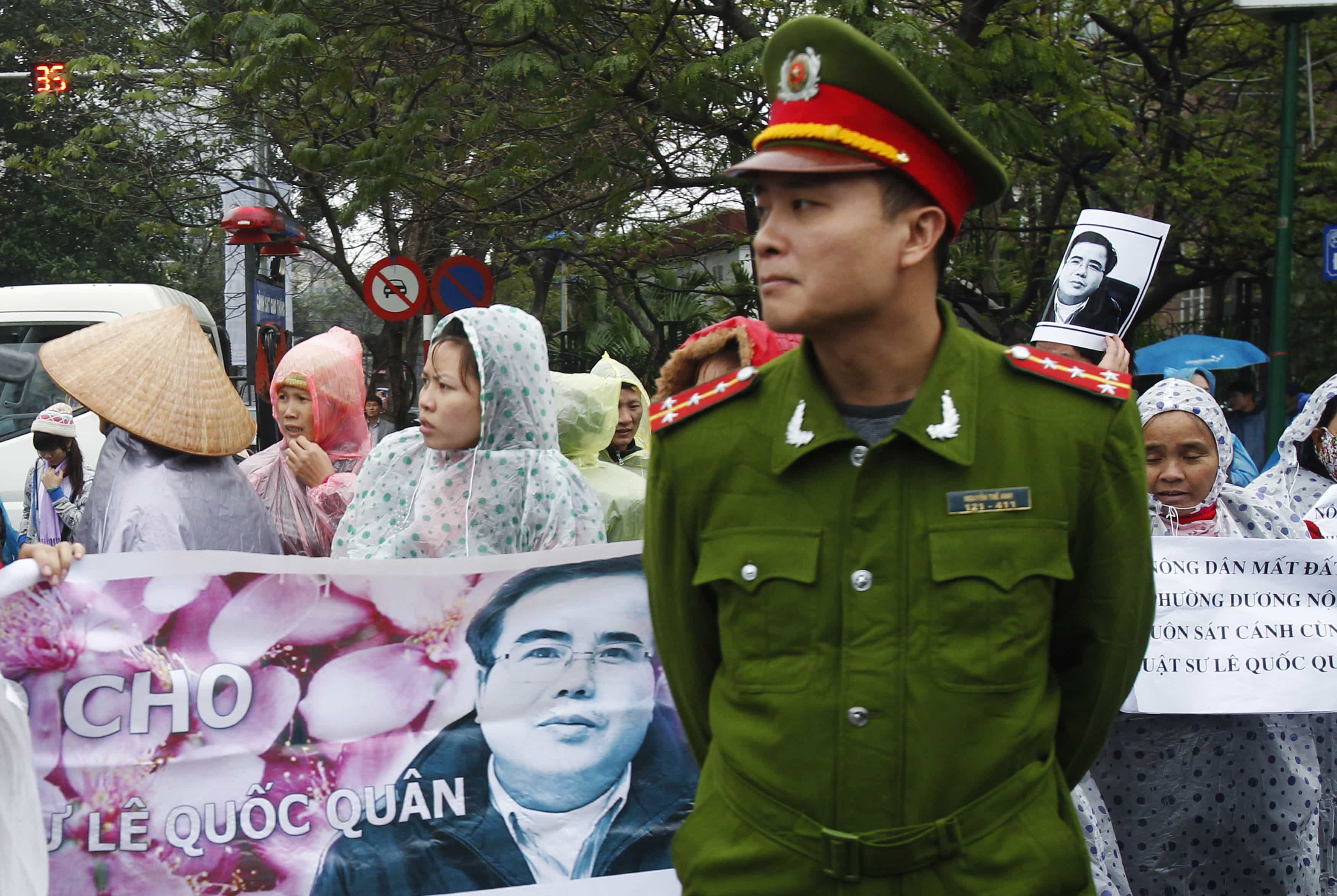 A policeman stands in front of supporters of lawyer Le Quoc Quan, as they hold a banner of him outside a court in Hanoi, REUTERS/Kham