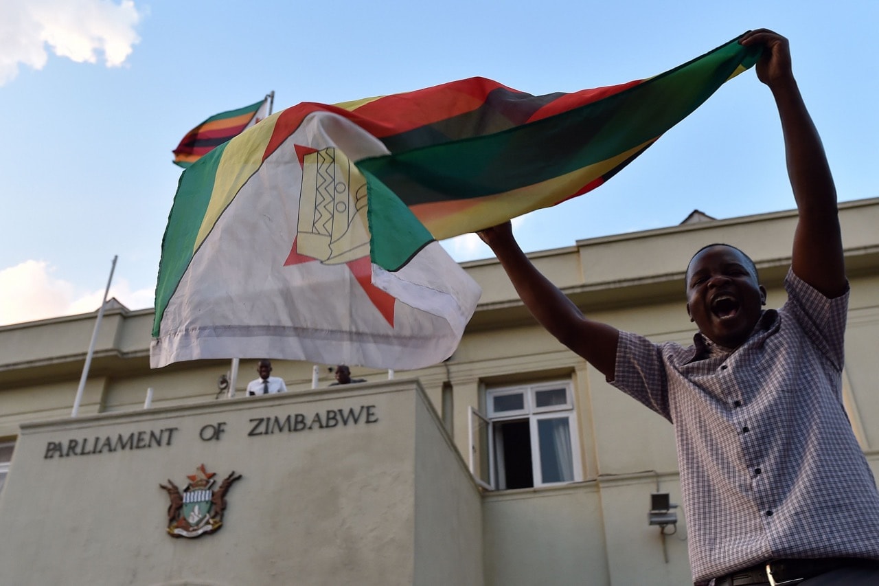 A man waves a flag as he celebrates the resignation of former president Robert Mugabe in front of the parliament in Harare, Zimbabwe, 21 November 2017, TONY KARUMBA/AFP/Getty Images