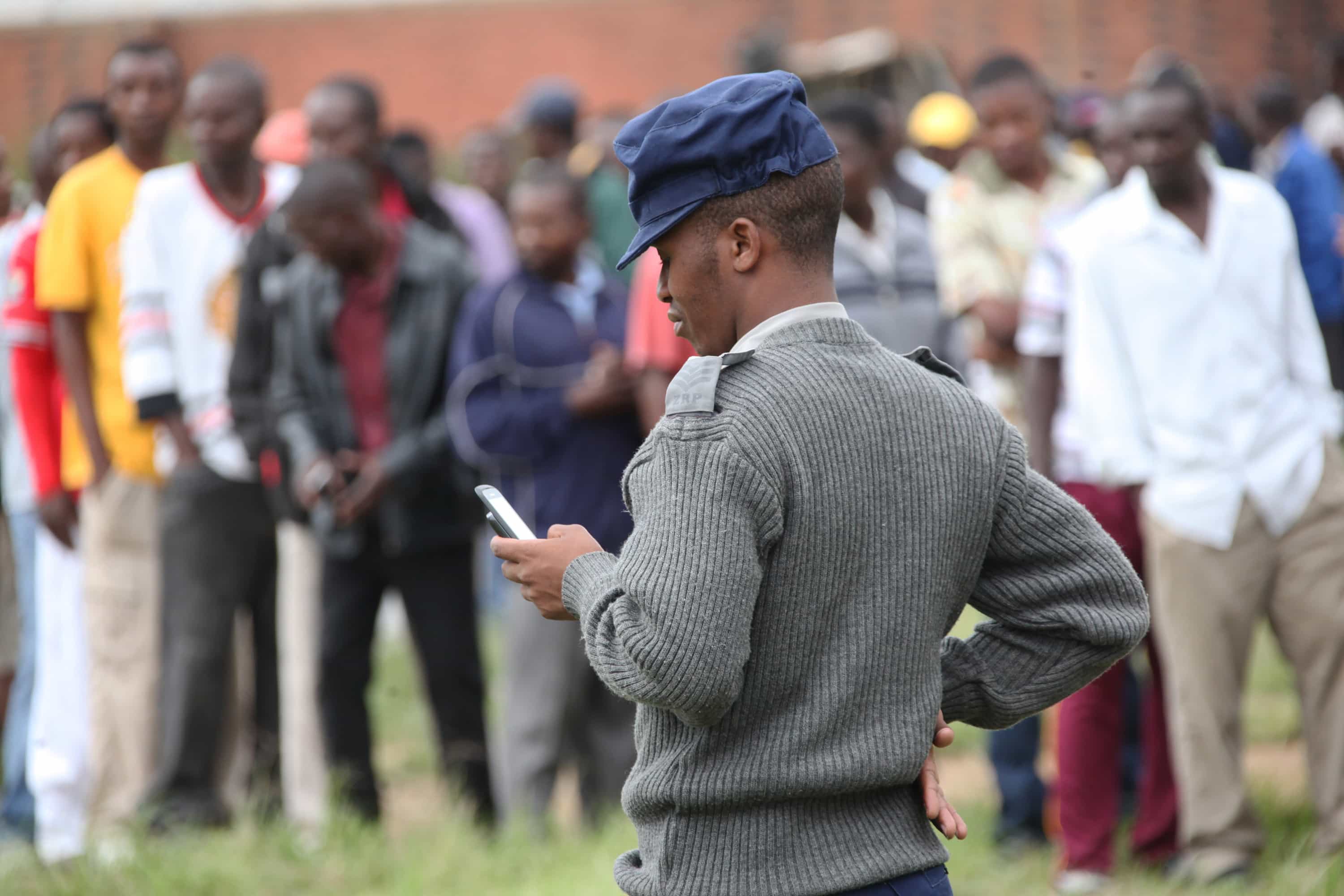 A police officer chats on a mobile phone at a polling station during a referendum in Harare, Zimbabwe, 16 March 2013, AP Photo/Tsvangirayi Mukwazhi