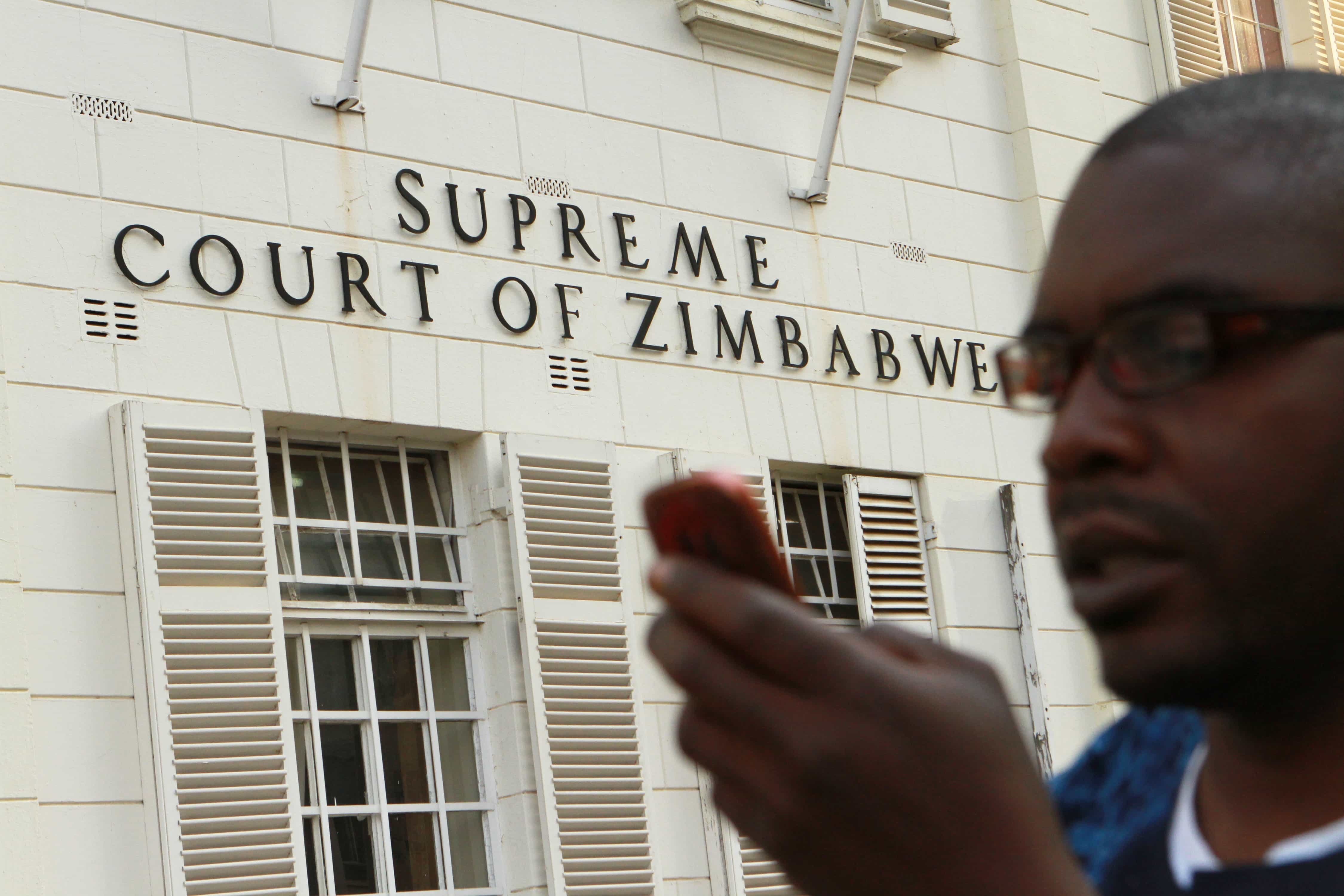 A journalist checks his mobile phone outside the Constitutional Court in Harare, 9 August 2013, AP Photo/Tsvangirayi Mukwazhi