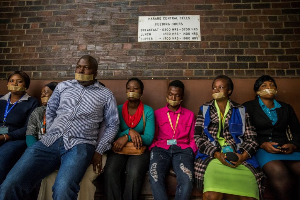 Zimbabwean journalists sit with their mouths taped to protest police methods at the Harare Central Police Station, 28 July 2017, JEKESAI NJIKIZANA/AFP/Getty Images