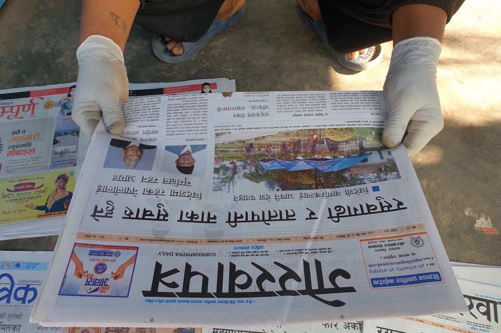 A man wearing protective gloves as a measure against COVID-19 looks at a newspaper, in Kathmandu, Nepal, 26 March 2020, Sunil Sharma/Xinhua via Getty