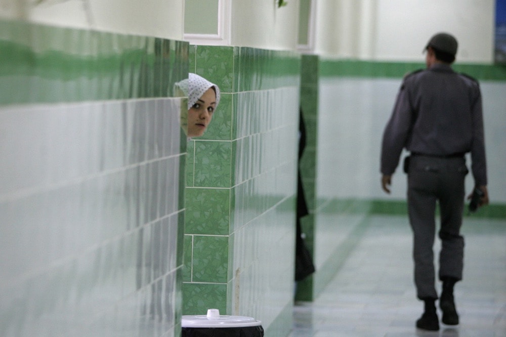 An inmate peers from behind a wall as a guard walks by in the female section of the infamous Evin prison, north of Tehran, Iran, 13 June 2006, ATTA KENARE/AFP via Getty Images