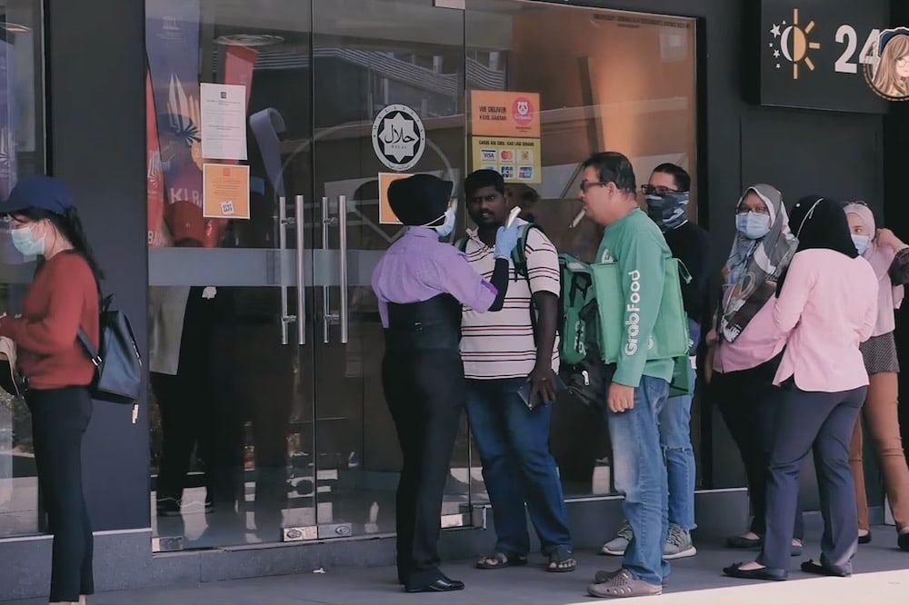 An employee at a fast food store checks the awaiting clients' temperature during the COVID-19 pandemic, Kuala Lumpur, Malaysia, 19 March 2020, 可恩Ke En, CC BY 3.0 , via Wikimedia Commons