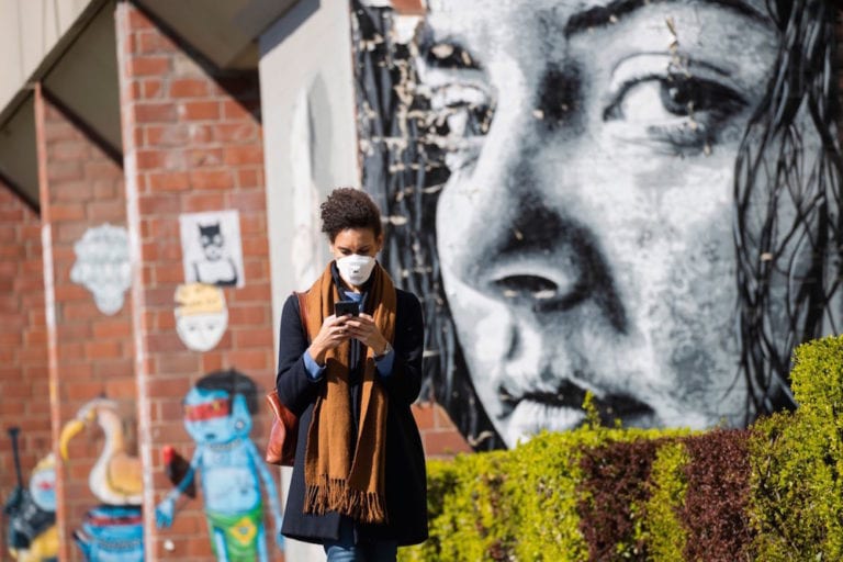 A woman looks at her smartphone while passing by a mural representing seeing eyes, Berlin, Germany, 1 April 2020, Emmanuele Contini/NurPhoto via Getty Images