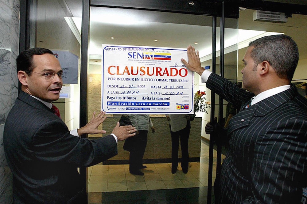 El presidente del Servicio Nacional Integrado de Administración Aduanera y Tributaria (Seniat) muestra un señal anunciando el cese de operaciones de una empresa, en Caracas, Venezuela, el 17 de marzo de 2006, ANDREW ALVAREZ/AFP via Getty Images