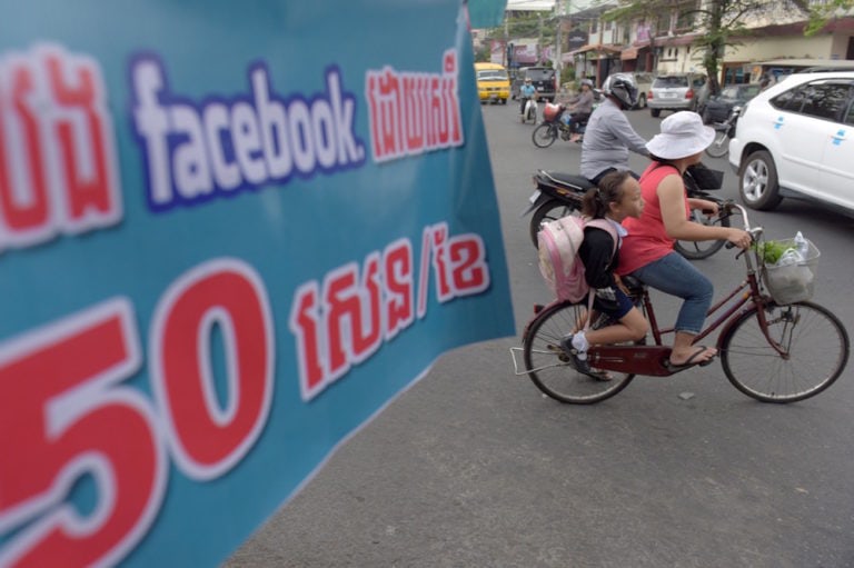 A woman cycles past a banner with a reference to Facebook and accessing the internet, in Phnom Penh, Cambodia, 22 March 2018, TANG CHHIN SOTHY/AFP via Getty Images