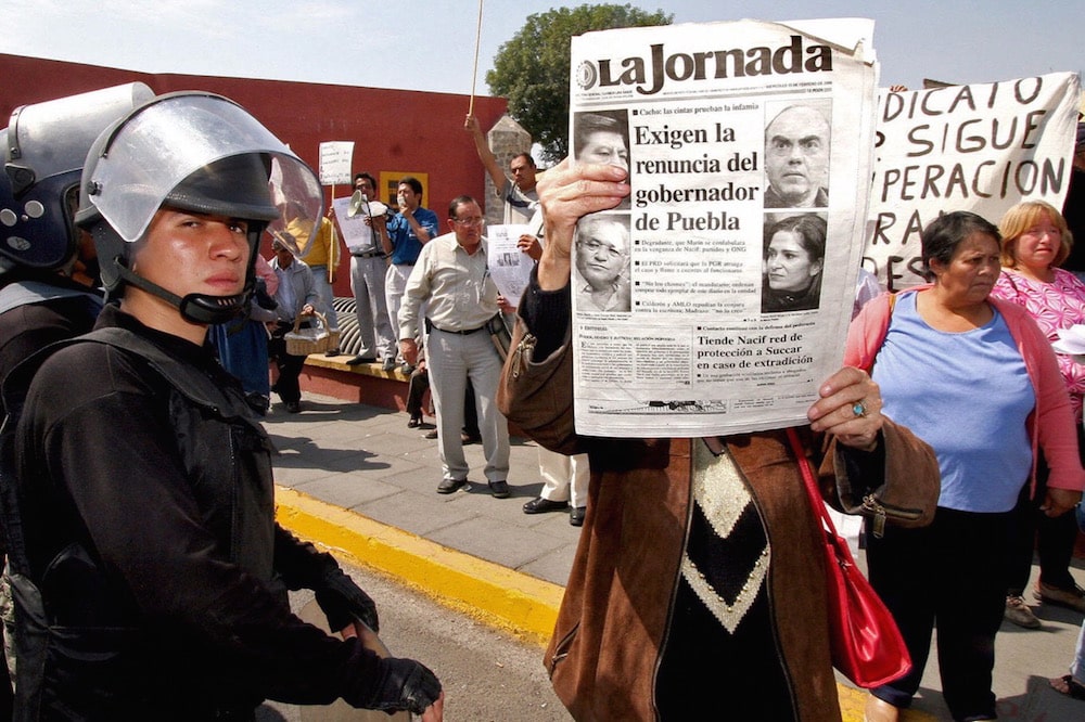 During a protest by dismissed employees from the local council, a woman holds up a newspaper with photos of Lydia Cacho and Mario Marín and the headline "Calls for the resignation of the Puebla governor", in Puebla, Mexico, 15 February 2005, Ronaldo Schemidt/AFP via Getty Images