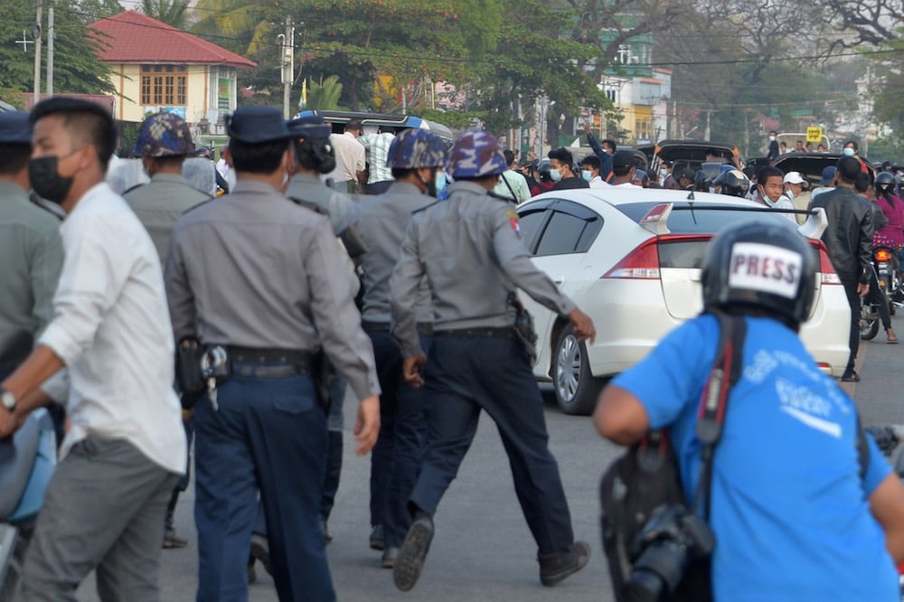 Riot police move in on protesters during a demonstration against the military coup as a journalist looks on, in Naypyidaw, Myanmar, 17 February 2021, STR/AFP via Getty Images