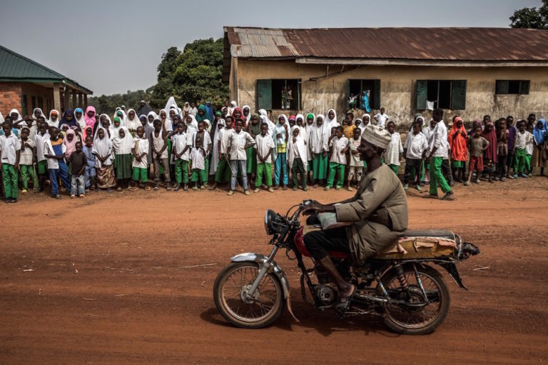 A man rides by on a motorcycle as a group of Fulani students gather at the entrance of their school in Kacha Grazing Reserve, Kaduna State, Nigeria, 19 April 2019, LUIS TATO/AFP via Getty Images