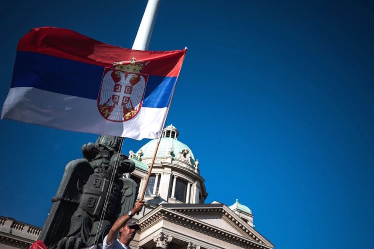 A man holds the Serbian national flag in front of the National assembly building in Belgrade, 18 June 2020, ANDREJ ISAKOVIC/AFP via Getty Images