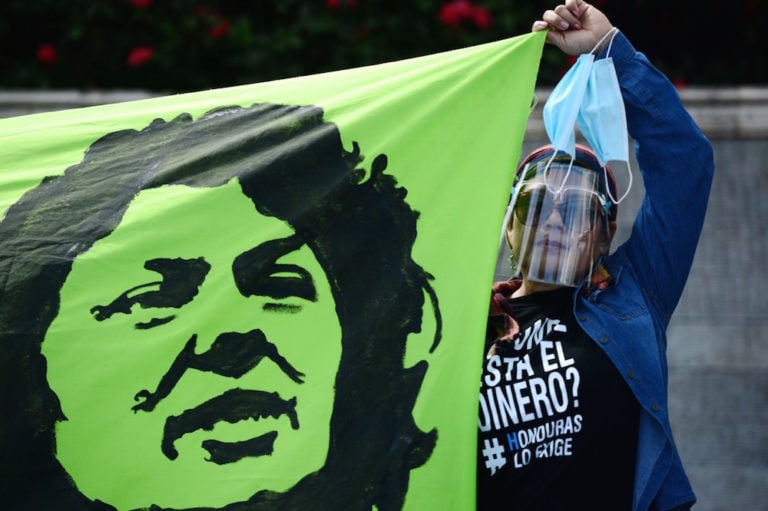 A woman holds a banner depicting murdered Honduran environmental activist Berta Cáceres during a protest calling for justice in her case, outside the Central-American Economic Integration Bank (BCIE), Tegucigalpa, Honduras, 3 October 2020, ORLANDO SIERRA/AFP via Getty Images