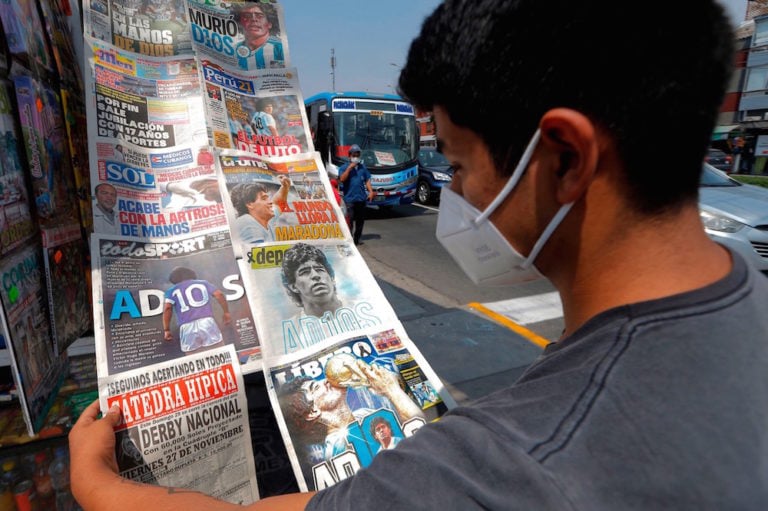 Un joven con una mascarilla mira las portadas de varios diarios en un quiosco, Buenos Aires, Argentina, el 26 de noviembre de 2020, LUKA GONZALES/AFP via Getty Images