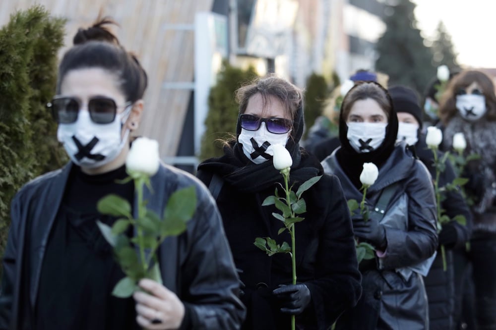 Women in black and with tape over their mouths hold white roses during a demonstration against the conviction of a doctor and journalist Katyarina Barisevich over the disclosure of a protester's medical records, Minsk, Belarus, 2 March 2021, STRINGER/AFP via Getty Images